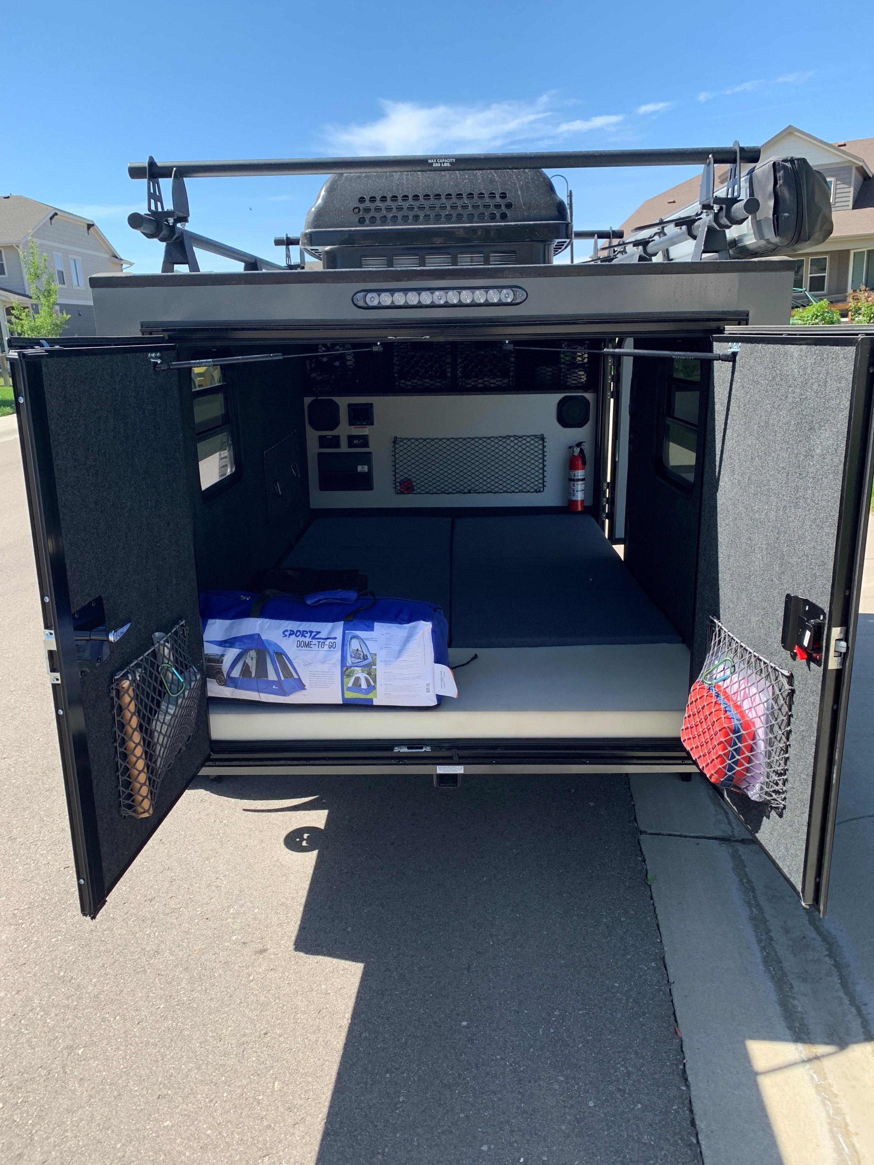 Open teardrop rv rental interior, featuring mattresses, storage, and a packed tent. Ready for your next outdoor adventure!. InTech RV Flyer 2022