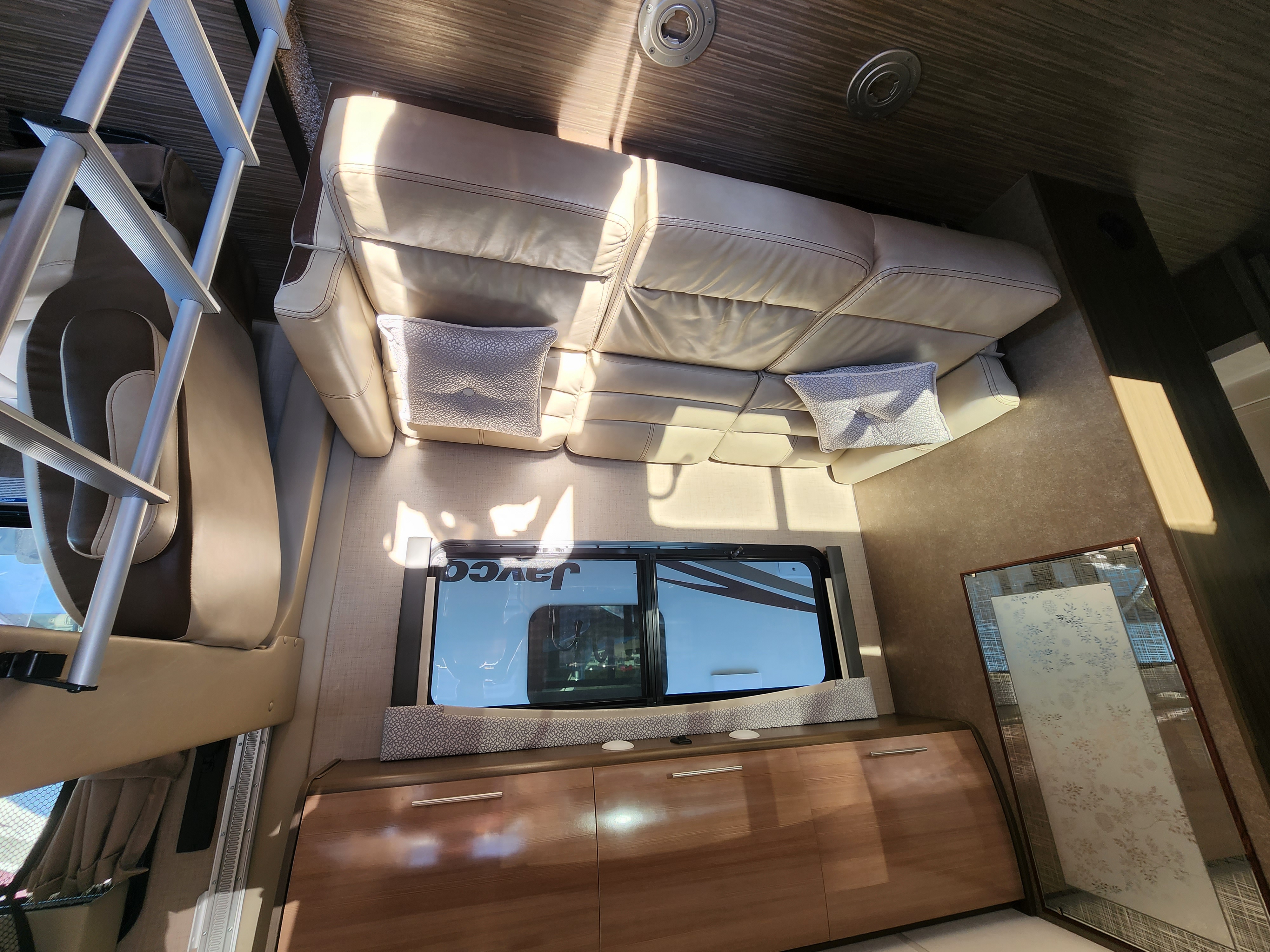 Bright RV rental interior with cream leather sofa, wooden cabinets, and a ladder for upper bunk access. Travel in comfort.. Thor Vegas 2019