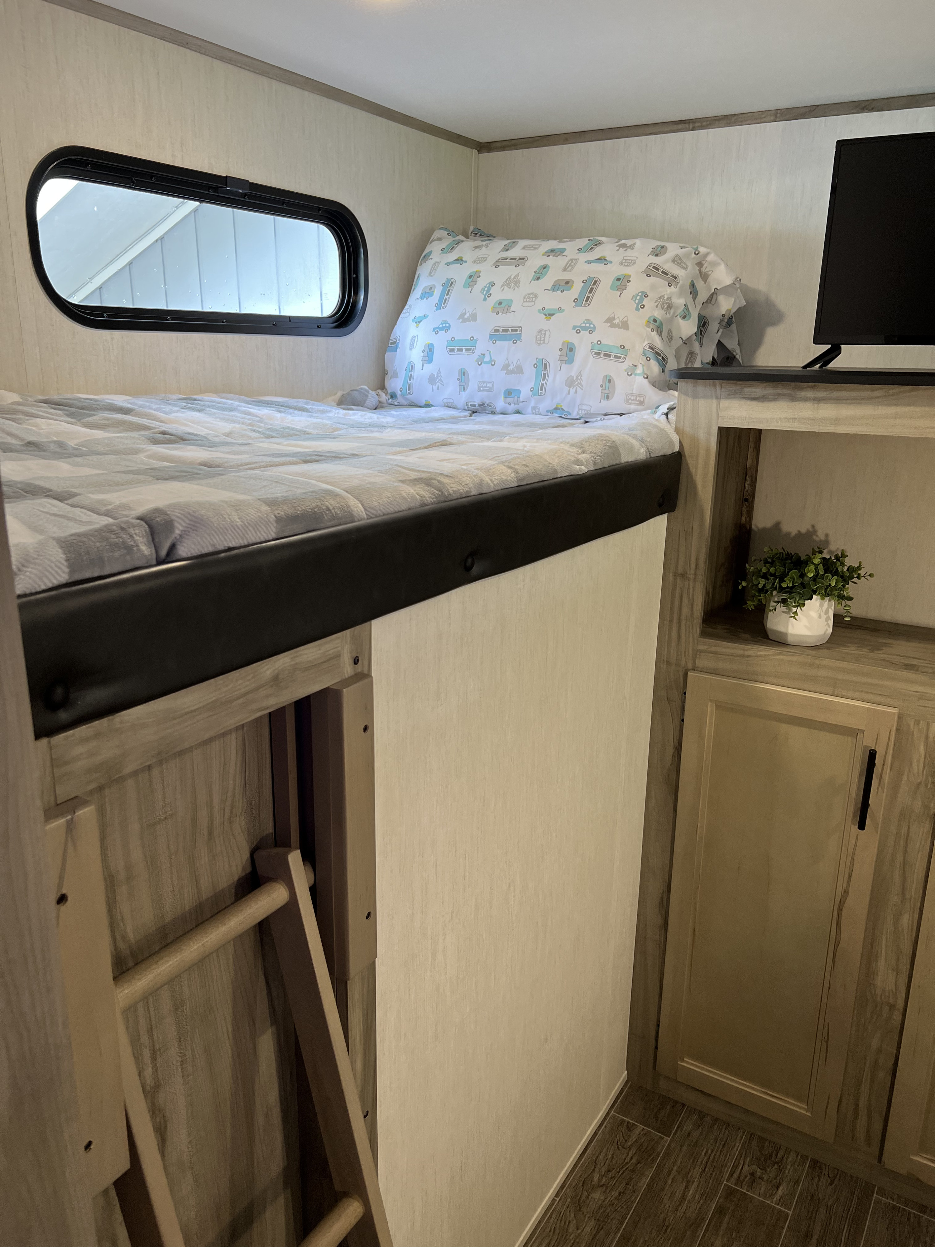 Cozy RV rental bunk bed with a window, access ladder, adjacent storage, and TV. Ideal for a comfortable road trip.. Forest River Cherokee Alpha Wolf 2022