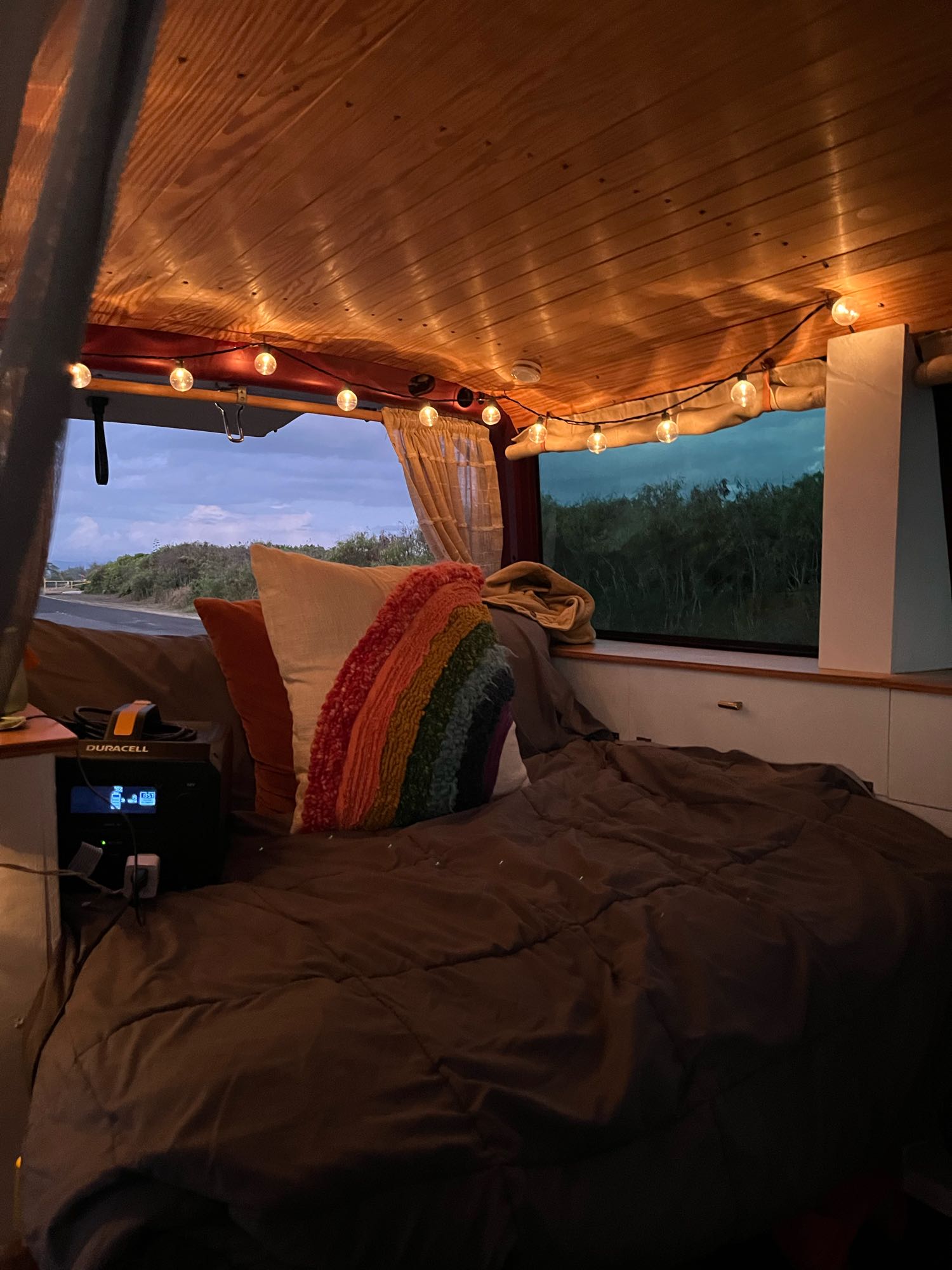 Inside a cozy RV rental: warm string lights, a comfy bed, and a power station with a tranquil evening view.. Volkswagen Eurovan 2003