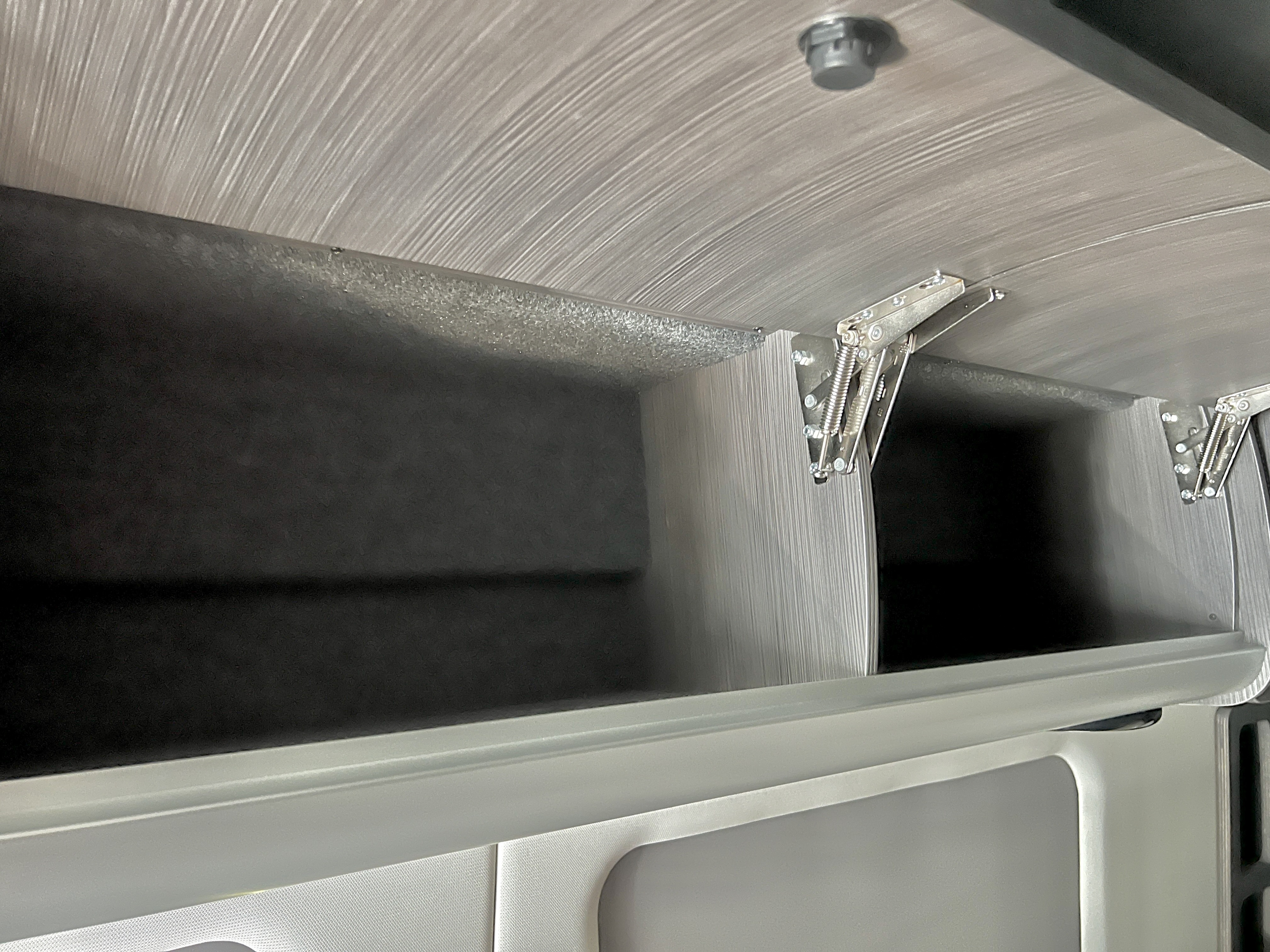 Overhead storage in this RV rental: spacious compartments with light wood-grain texture, dark interiors, and strong spring hinges.. Airstream Interstate 2021