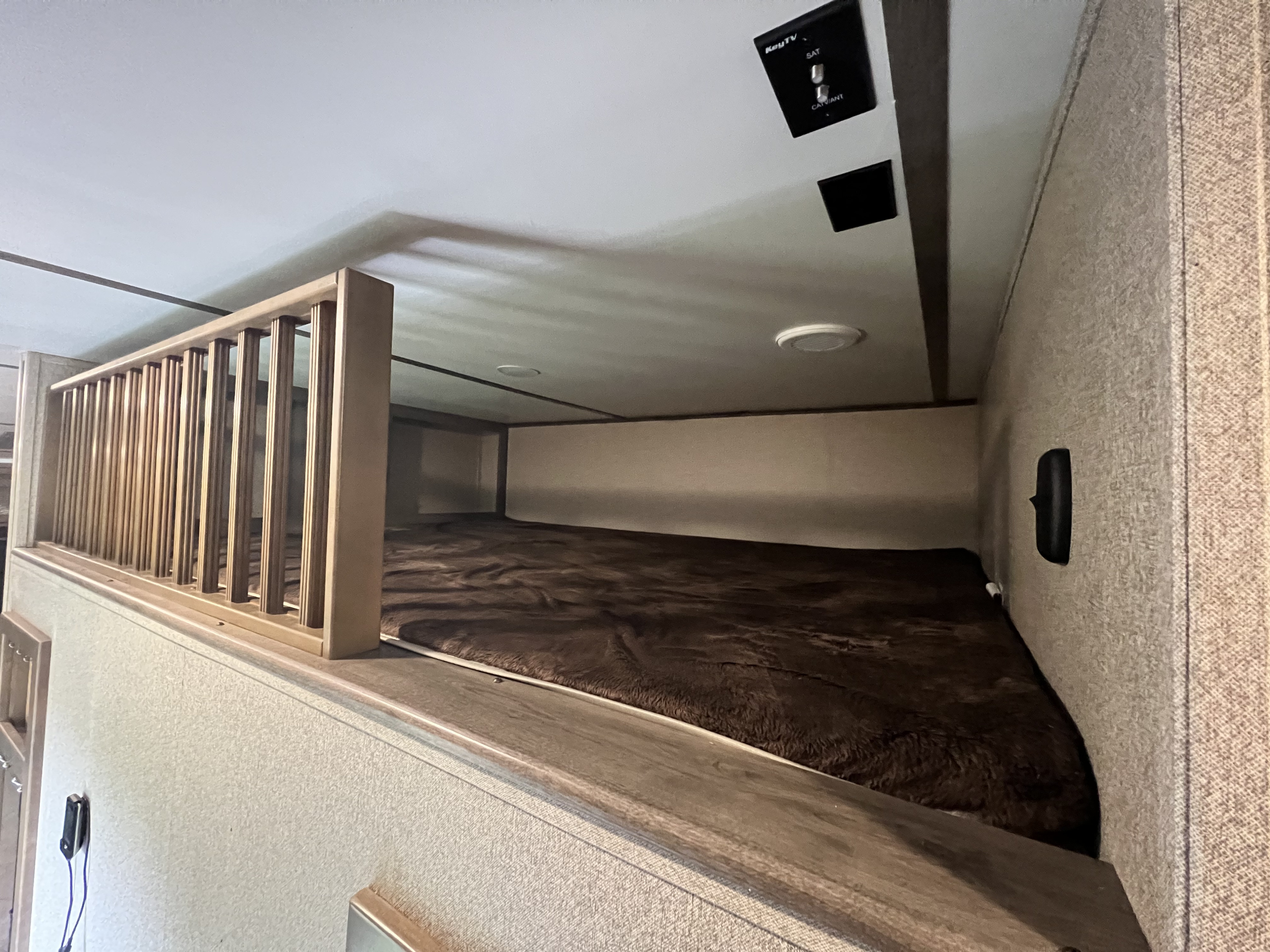 RV rental: Elevated bunk bed with wooden safety railing and cozy brown blanket, offering extra sleeping space.. Keystone Sprinter 2019