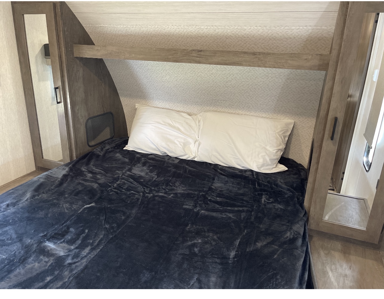 Well-appointed RV rental bedroom with a plush bed, white pillows, dark blanket, and convenient mirrored closets.. Forest River Wildwood 2022