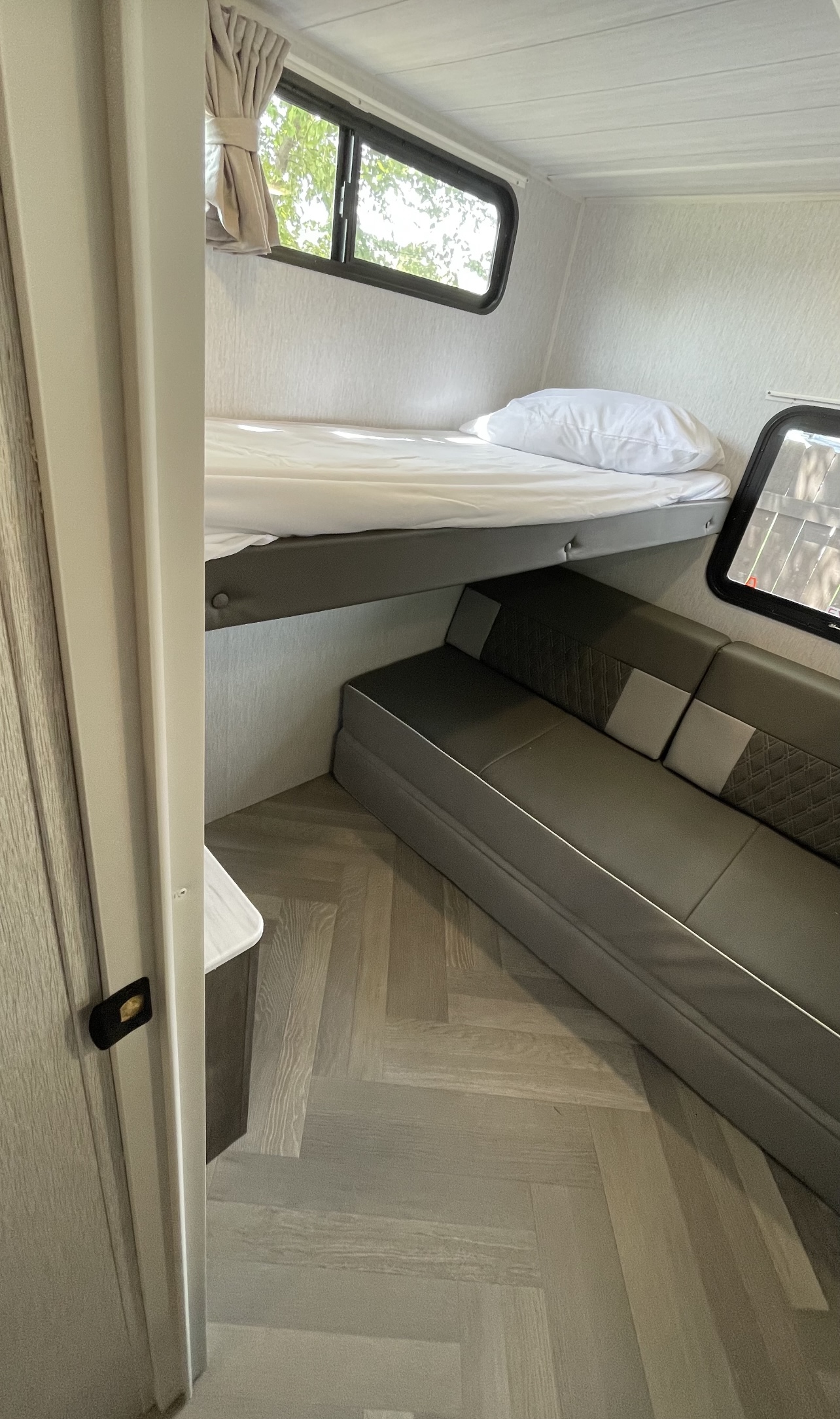 Inside an RV rental, a cozy bunk bed sits above a plush couch. A window offers natural light over wood-look flooring.. Forest River Wildwood 2022