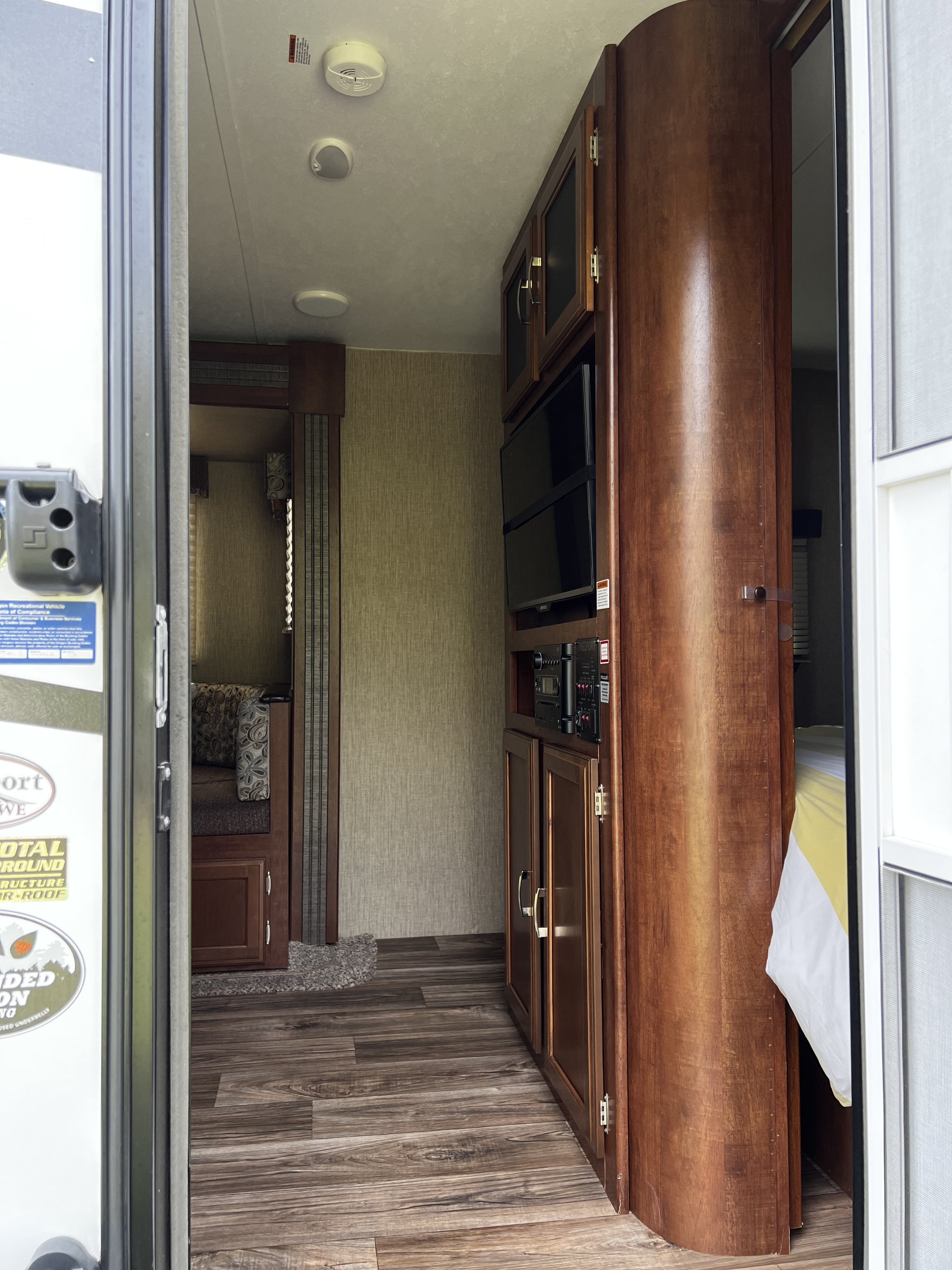 View inside an RV rental: dinette, wood entertainment unit with TV, and bedroom visible in the compact living space.. Keystone RV Passport Grand Touring 2016