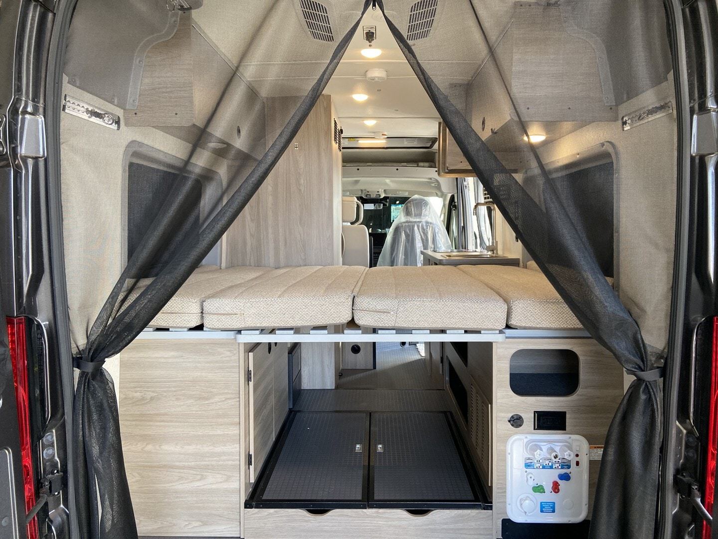 Inside this RV rental camper van: an elevated bed with storage below, framed by a mosquito net at the rear. Adventure awaits!. WINNIBAGO SOLIS 2023
