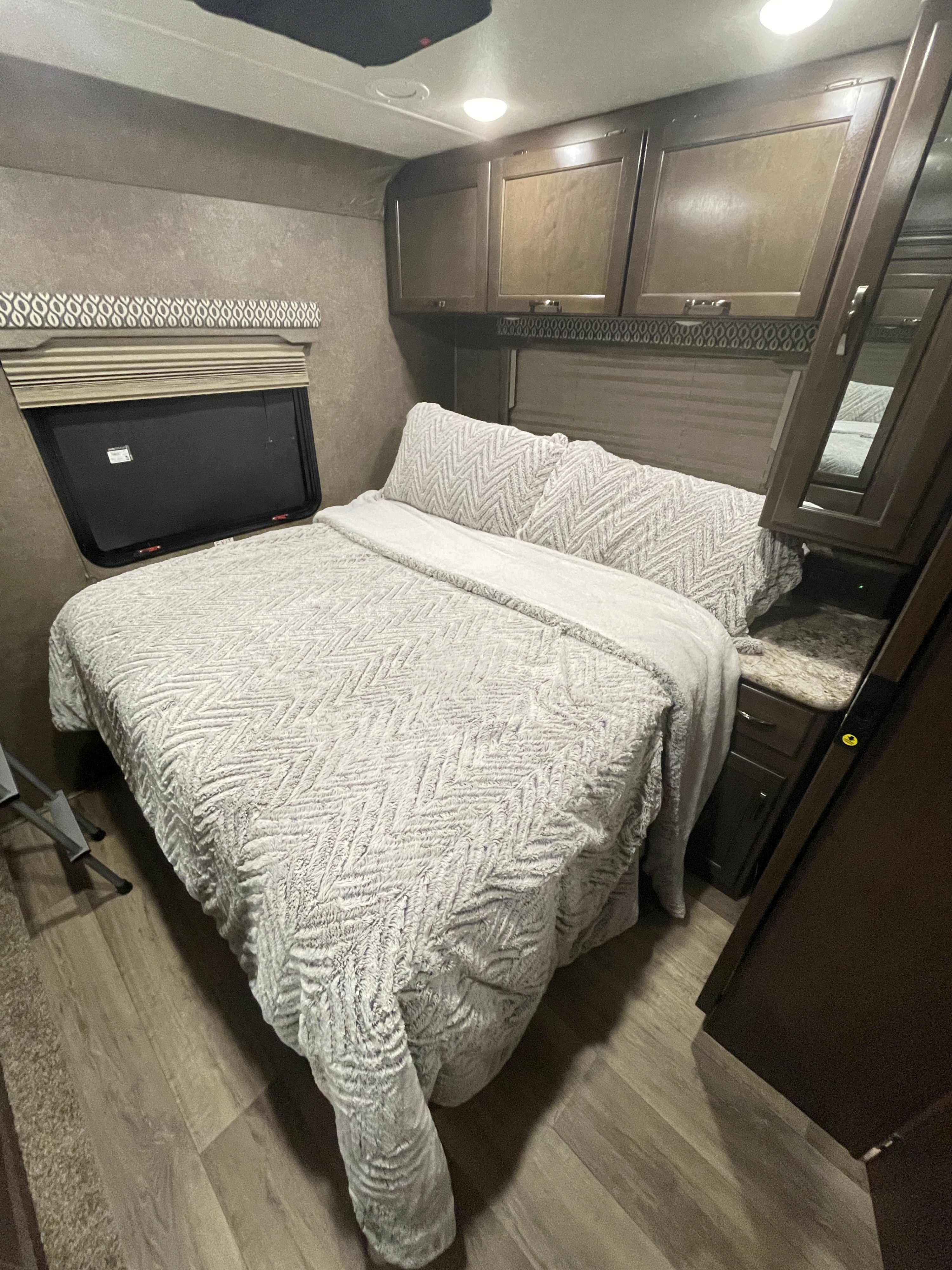 Cozy RV rental bedroom with a grey chevron comforter, window, and wood cabinetry. Ready for your adventure.. Thor Freedom Elite 2020
