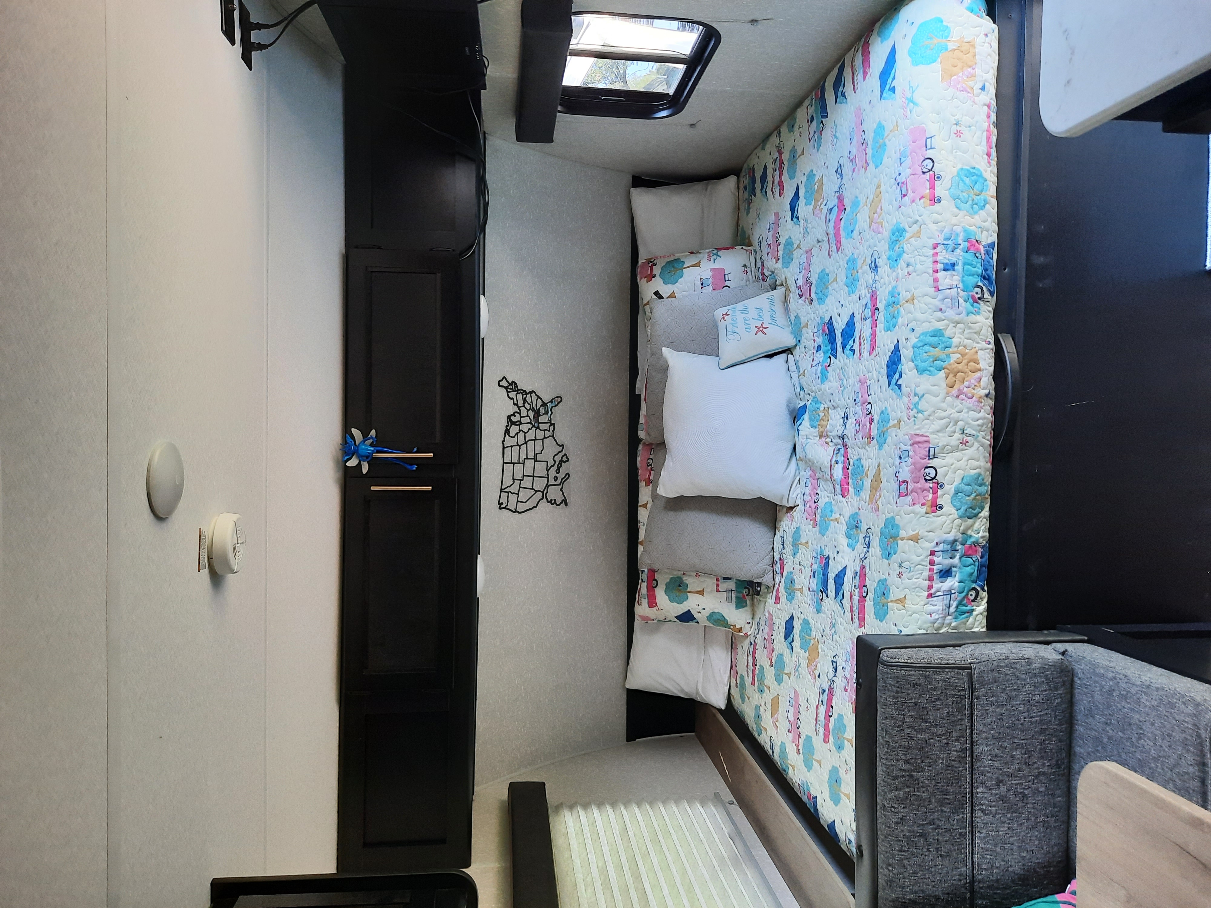 RV rental interior: a cozy bedroom with a patterned quilt, multiple pillows, dark cabinet, and small window, ideal for travel.. Forest River Cherokee Wolf Pup 2022