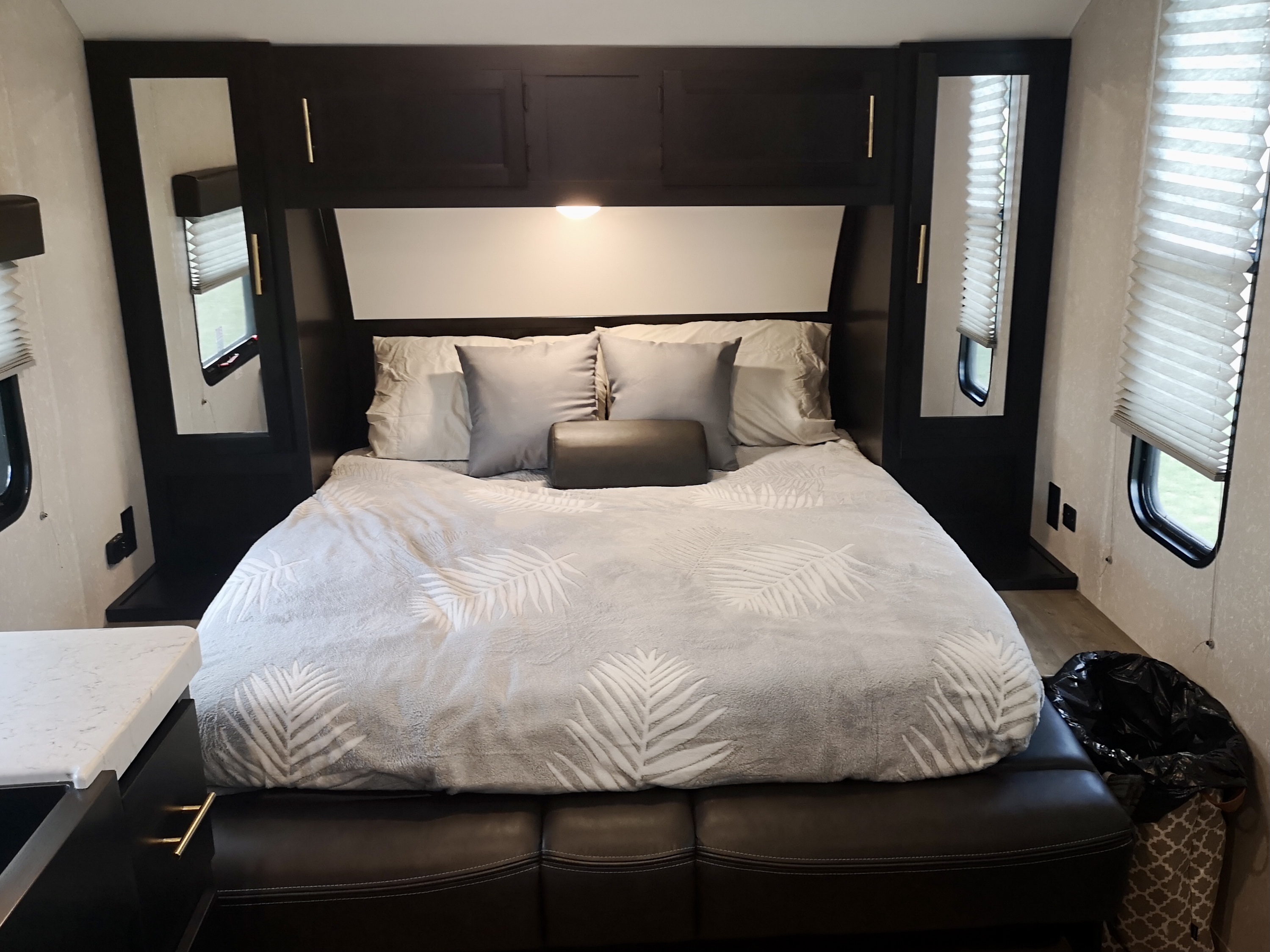 Cozy RV rental bedroom features a comfortable bed with palm-patterned bedding, dark built-in cabinets, and window blinds.. Forest River Cherokee Grey Wolf 2022