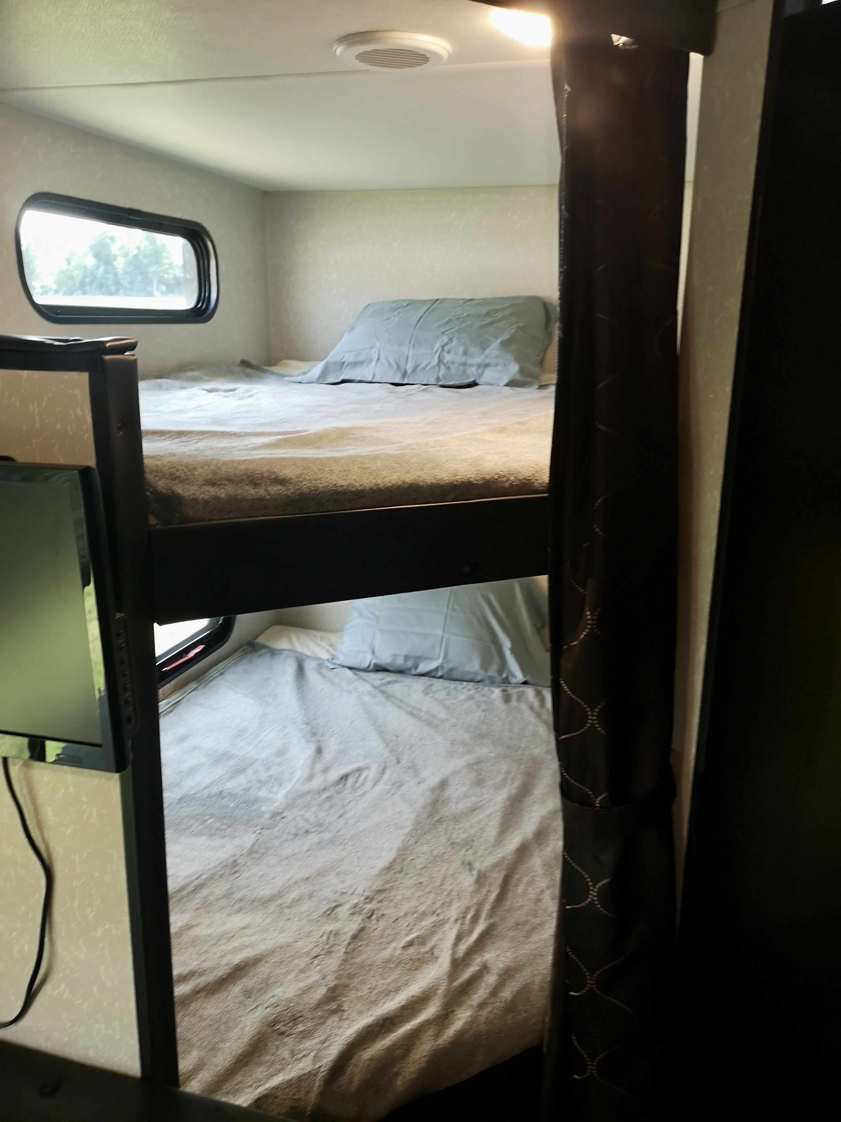 Cozy bunk beds inside an RV rental, complete with a window, ceiling vent, and TV. Ideal travel accommodation.. Forest River Cherokee Grey Wolf 2022