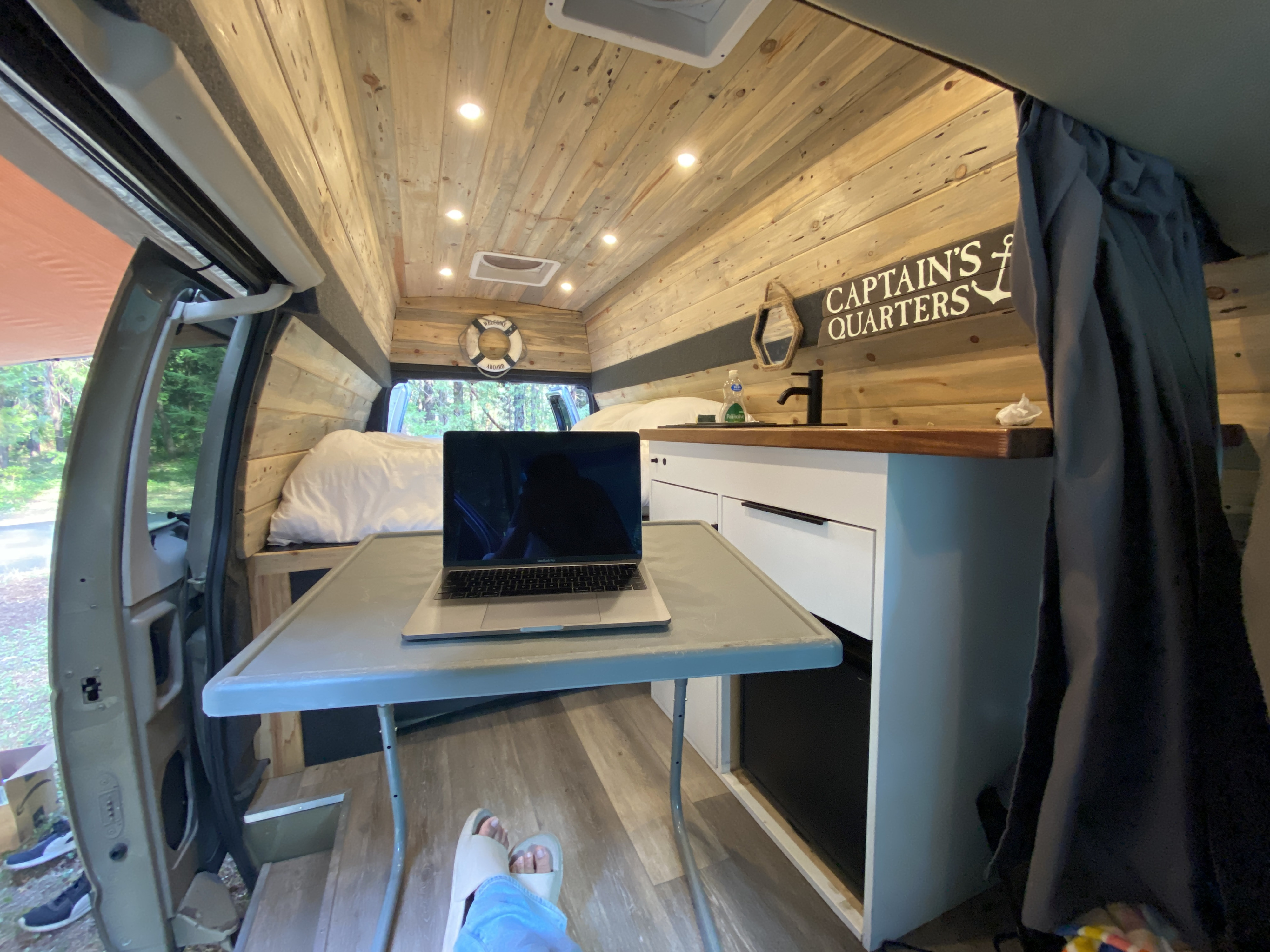 Cozy RV rental interior showing wooden walls/ceiling, laptop on table, and bed. Ideal for remote work/van life.. Ford Econoline E350 Extended 2004