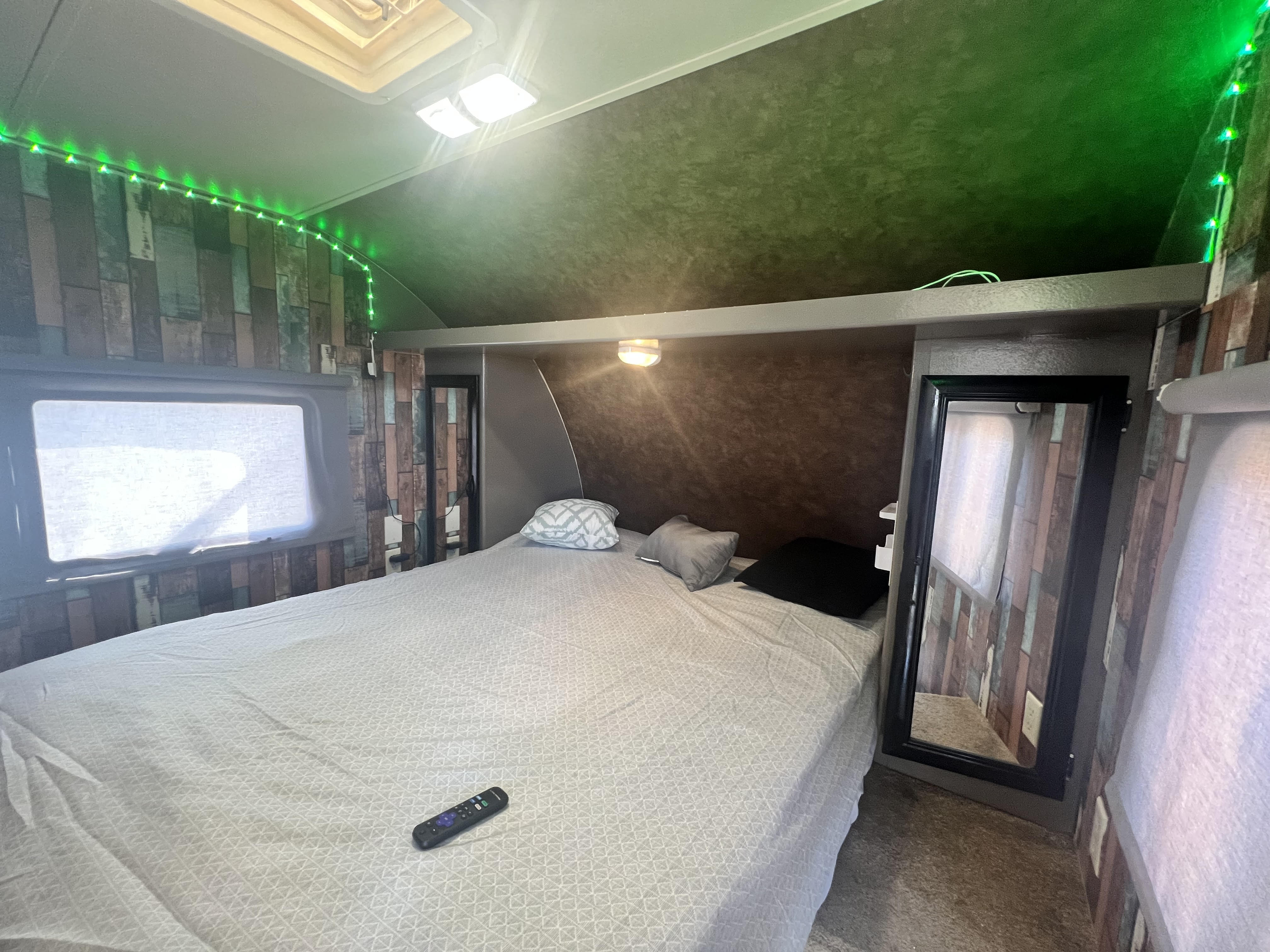 Cozy RV rental bedroom featuring a large bed, window with shade, green LED string lights, and stylish wood-look walls.. Forest River Salem Cruise Lite 2014