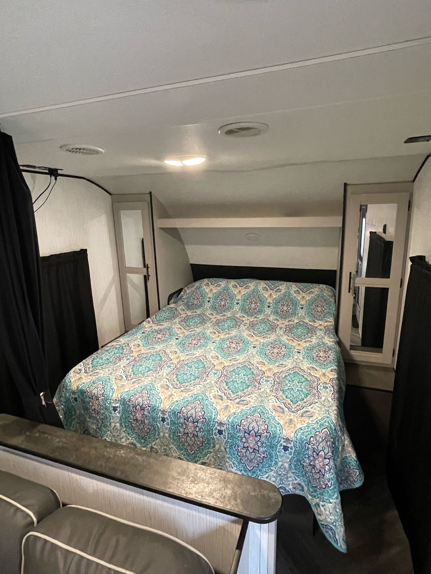 Cozy RV rental bedroom featuring a bed with a patterned quilt, overhead storage, and partial seating area in the foreground.. Heartland RVs Prowler 2021