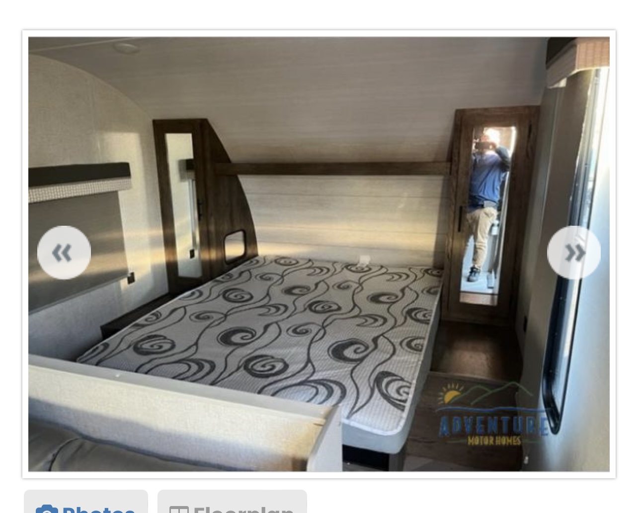 Inside an RV rental: a compact bedroom features a patterned bed, mirrored door, and cozy wood interior.. Forest River Wildwood X-Lite 2021