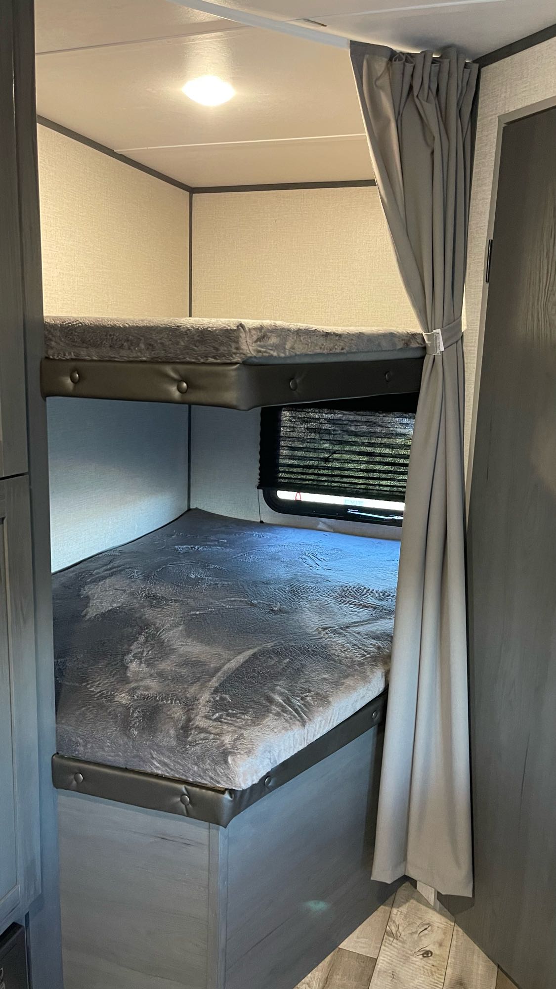 RV rental bunk beds: comfortable upper and lower bunks with soft gray bedding, a window with blinds, and a privacy curtain.. Aspen Trail LE 2022