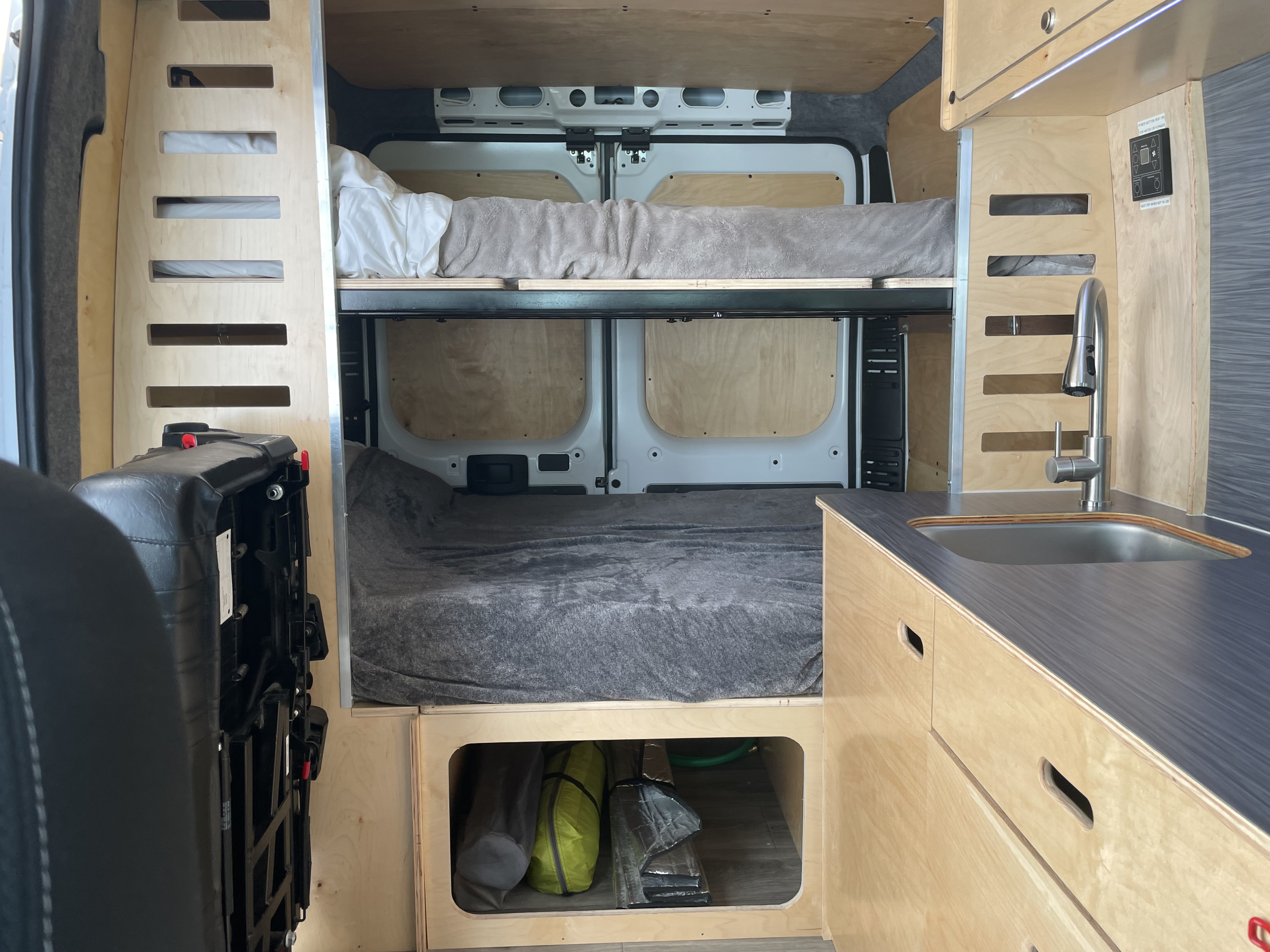 Custom camper van RV rental interior featuring two bunk beds, a compact kitchen with sink, and under-bed storage.. RAM ProMaster 2022