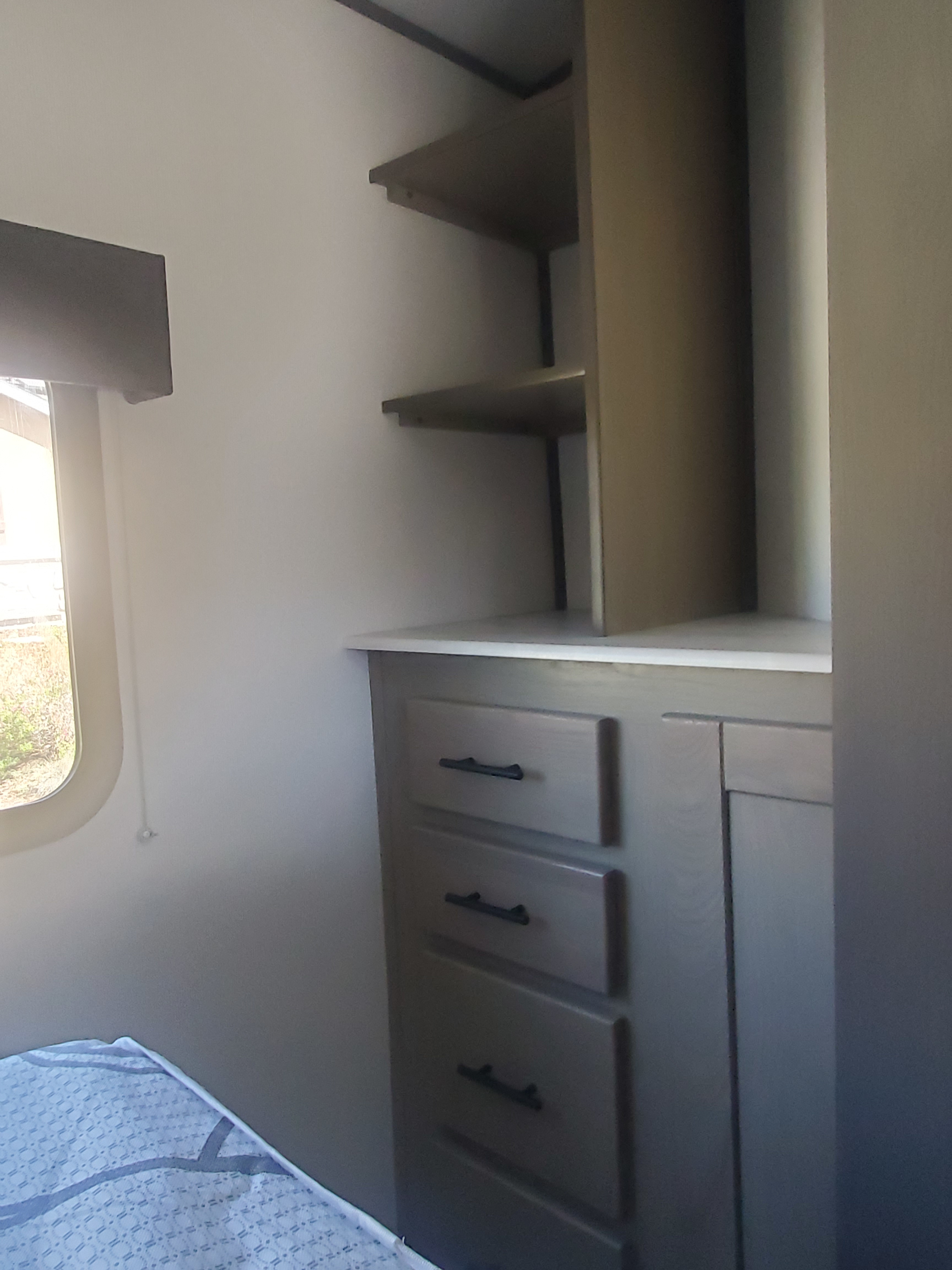 RV rental bedroom featuring a built-in dresser with drawers, open shelves, and a window for comfortable living.. Cruiser RV Shadow Cruiser 2022