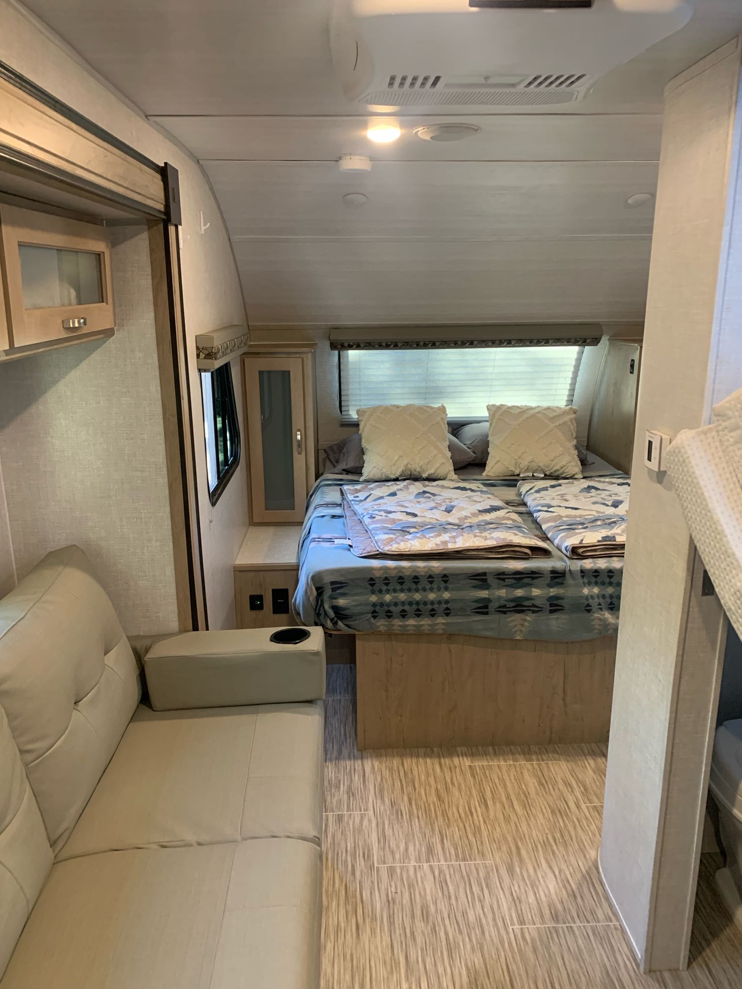Cozy rv rental interior featuring a bed with patterned blankets, a small sofa with cup holder, and modern wood-look flooring.. R-Pod Hood River Edition 2020