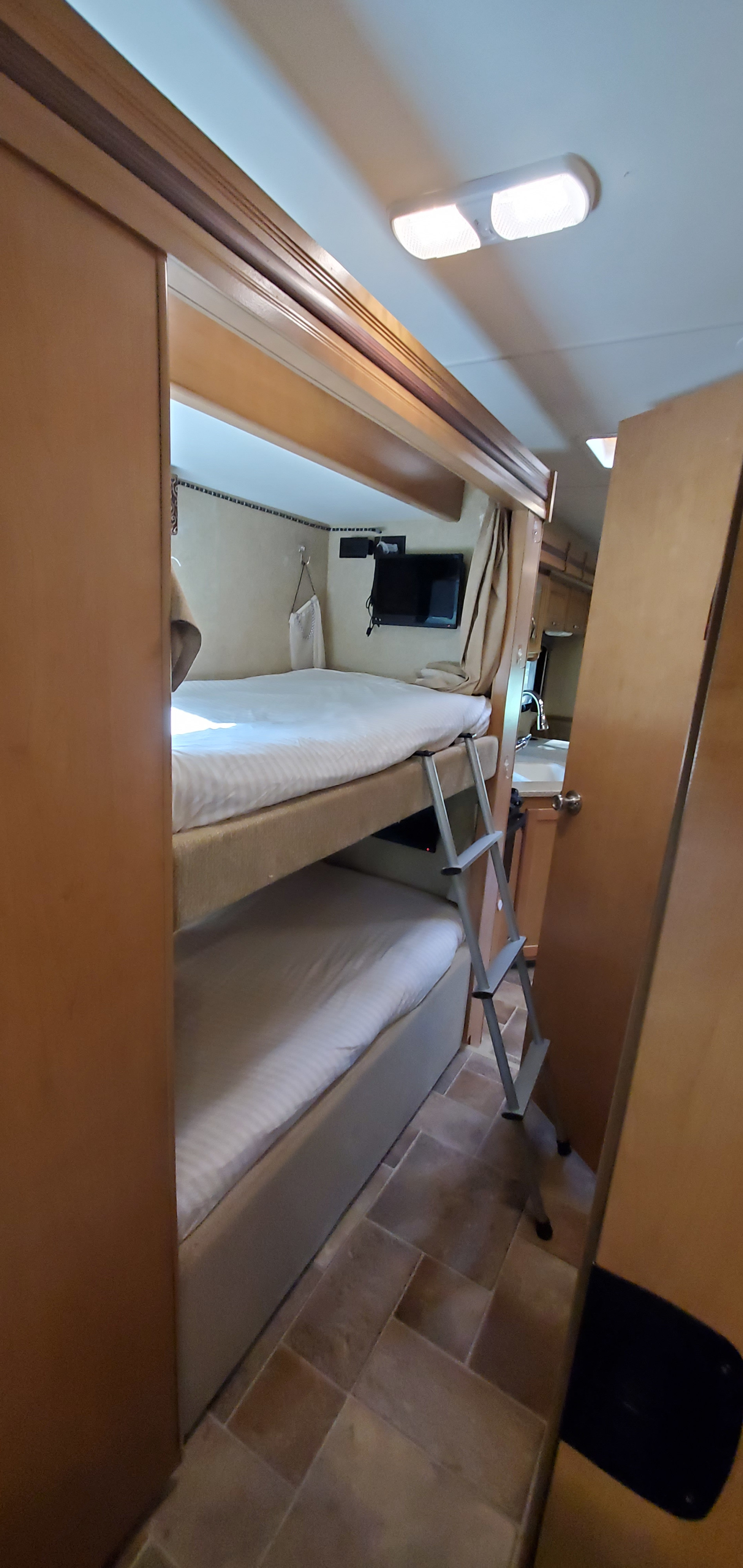 RV rental's functional interior: double bunk beds with ladder, TV, and compact kitchen. Ready for road trips!. Thor Four Winds 31E 2015