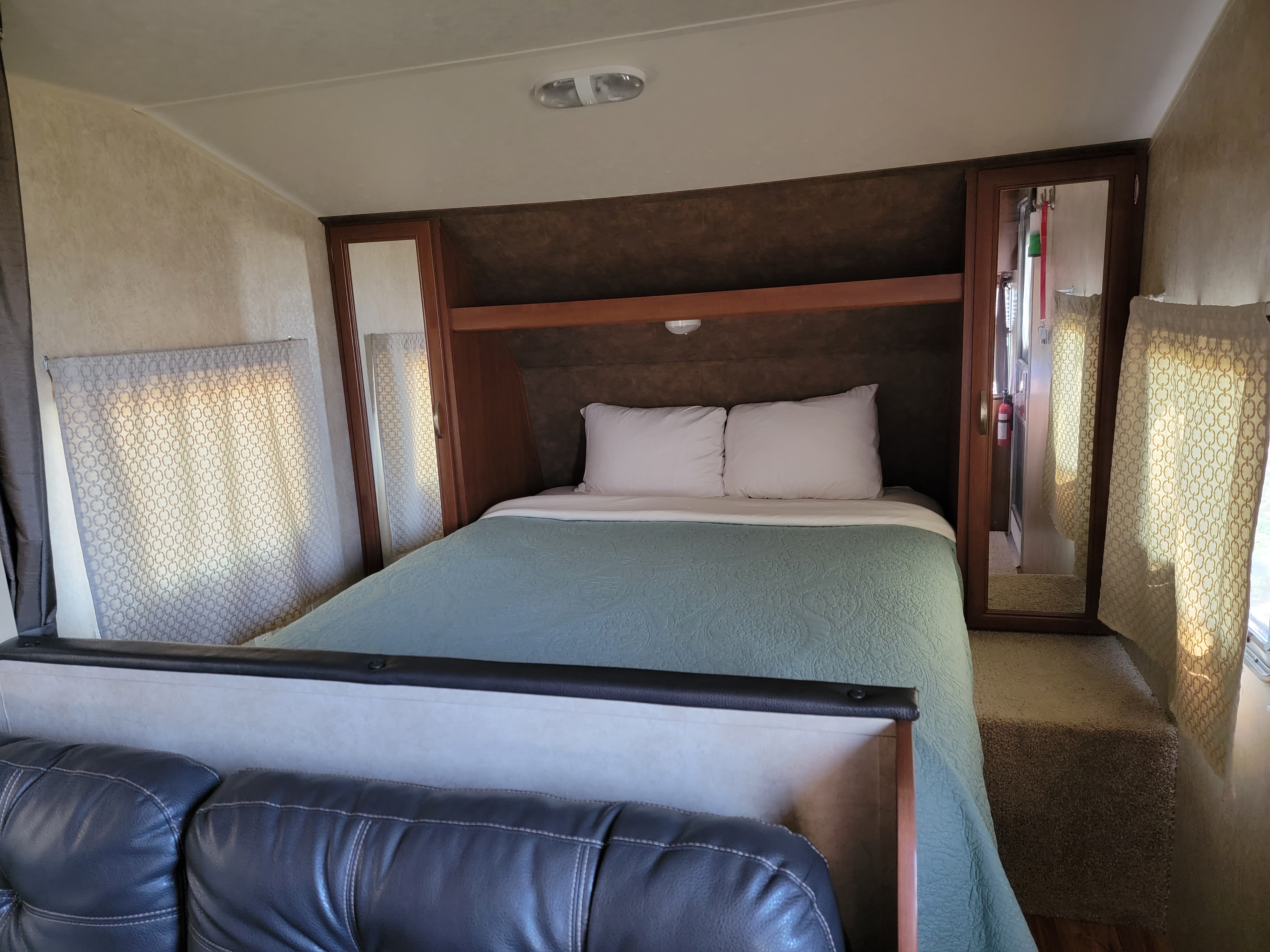 Interior of an RV rental bedroom showing a bed, mirrored closets, and patterned windows, offering a comfortable stay.. Forest River Salem Cruise Lite 2014