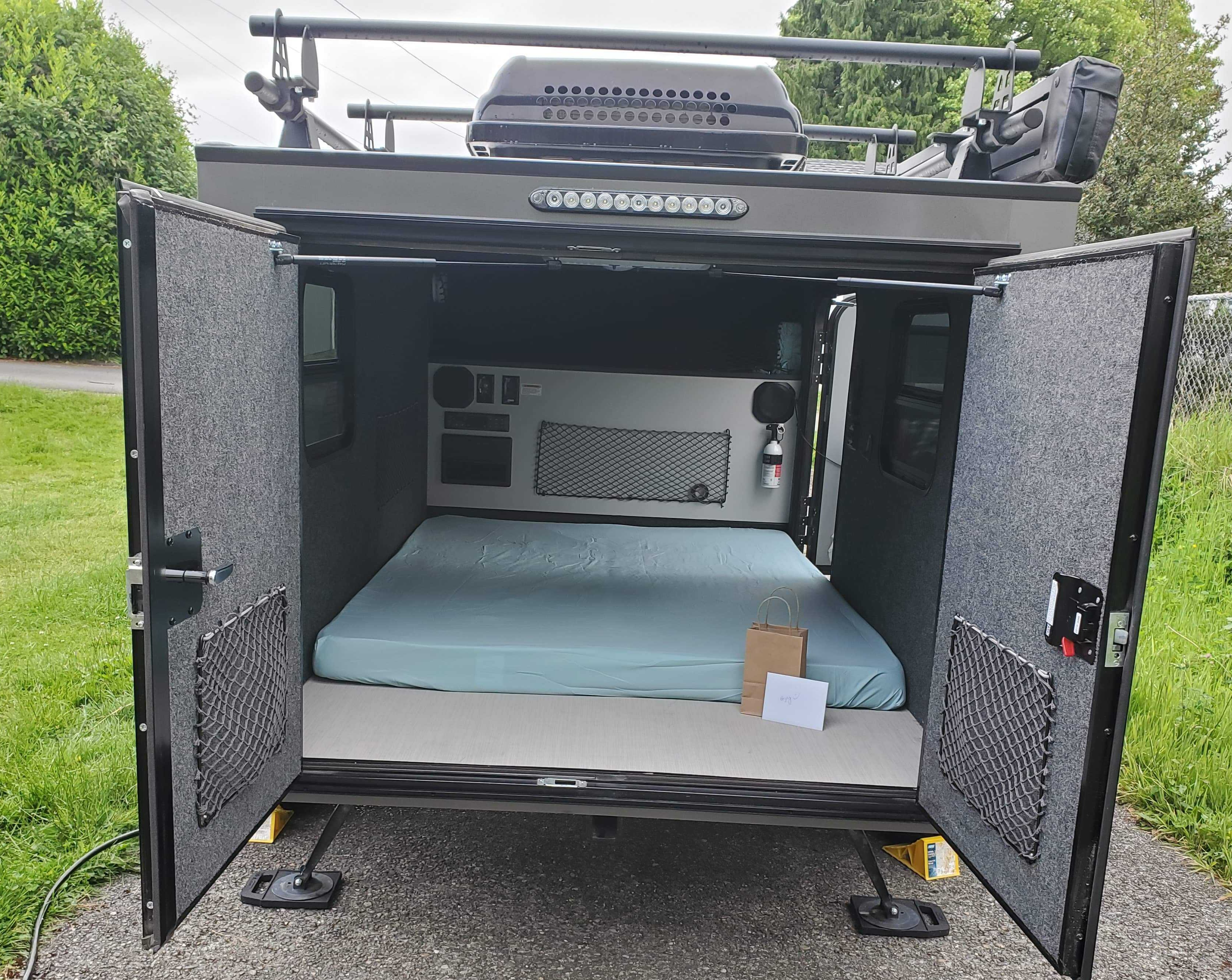 Compact RV rental interior seen through open rear hatch, showing bed, controls, and storage.. Intech Flyer Pursue 2020