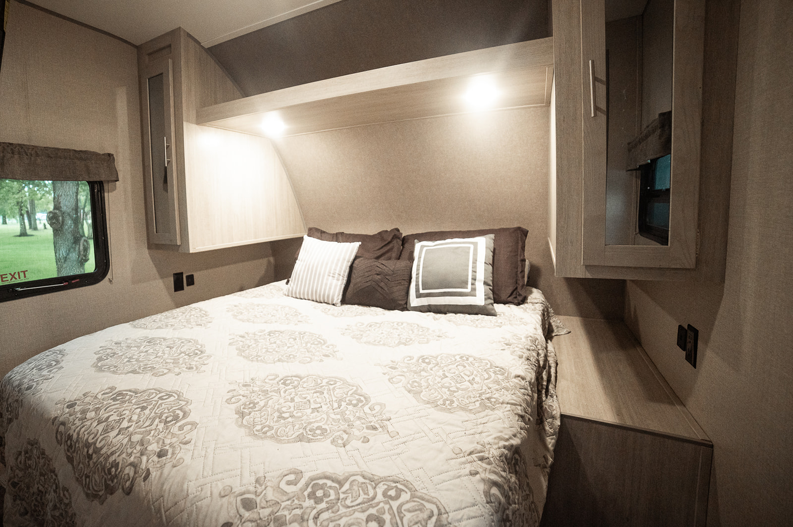 Cozy RV rental bedroom featuring a comfy bed with decorative bedding, overhead cabinets, and a window overlooking trees.. Forest River Coachmen Aurora 2022