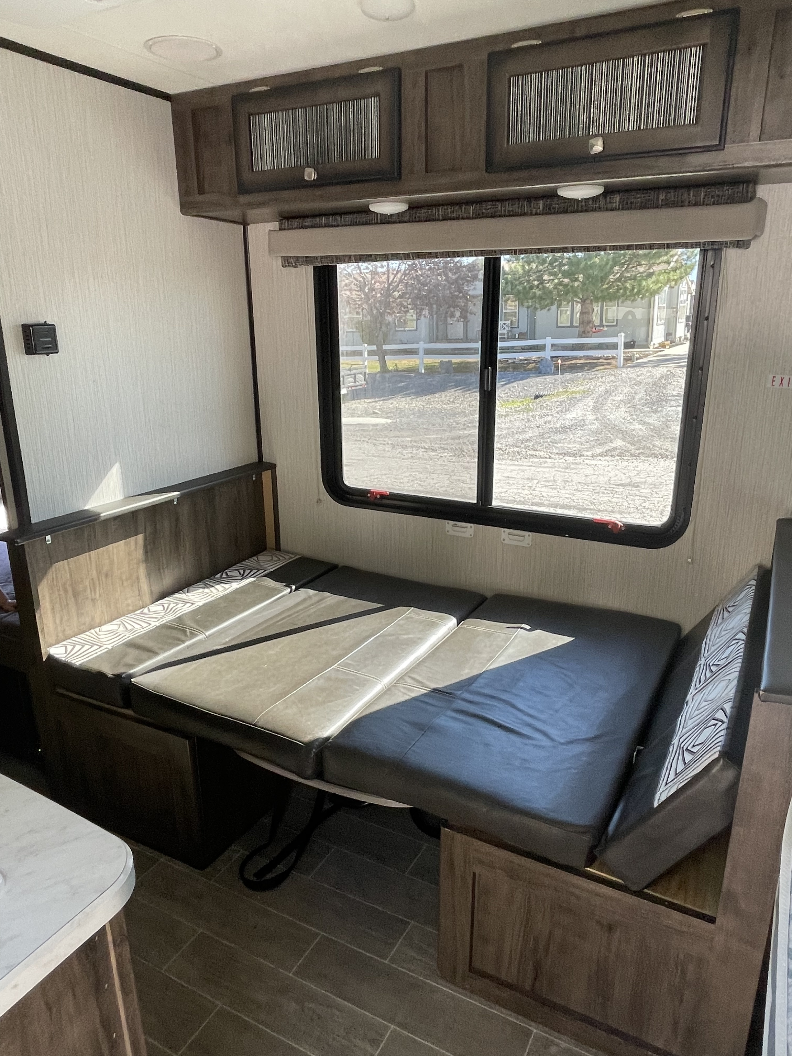 RV rental interior: a versatile dinette converts to a bed with dark cushions, under overhead cabinets, beside a window.. Other Other 2020