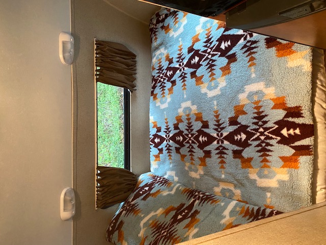 Cozy RV rental interior showing an Aztec-patterned blanket on a bed and a window revealing green grass outside.. Forest River Hood River R Pod 2013