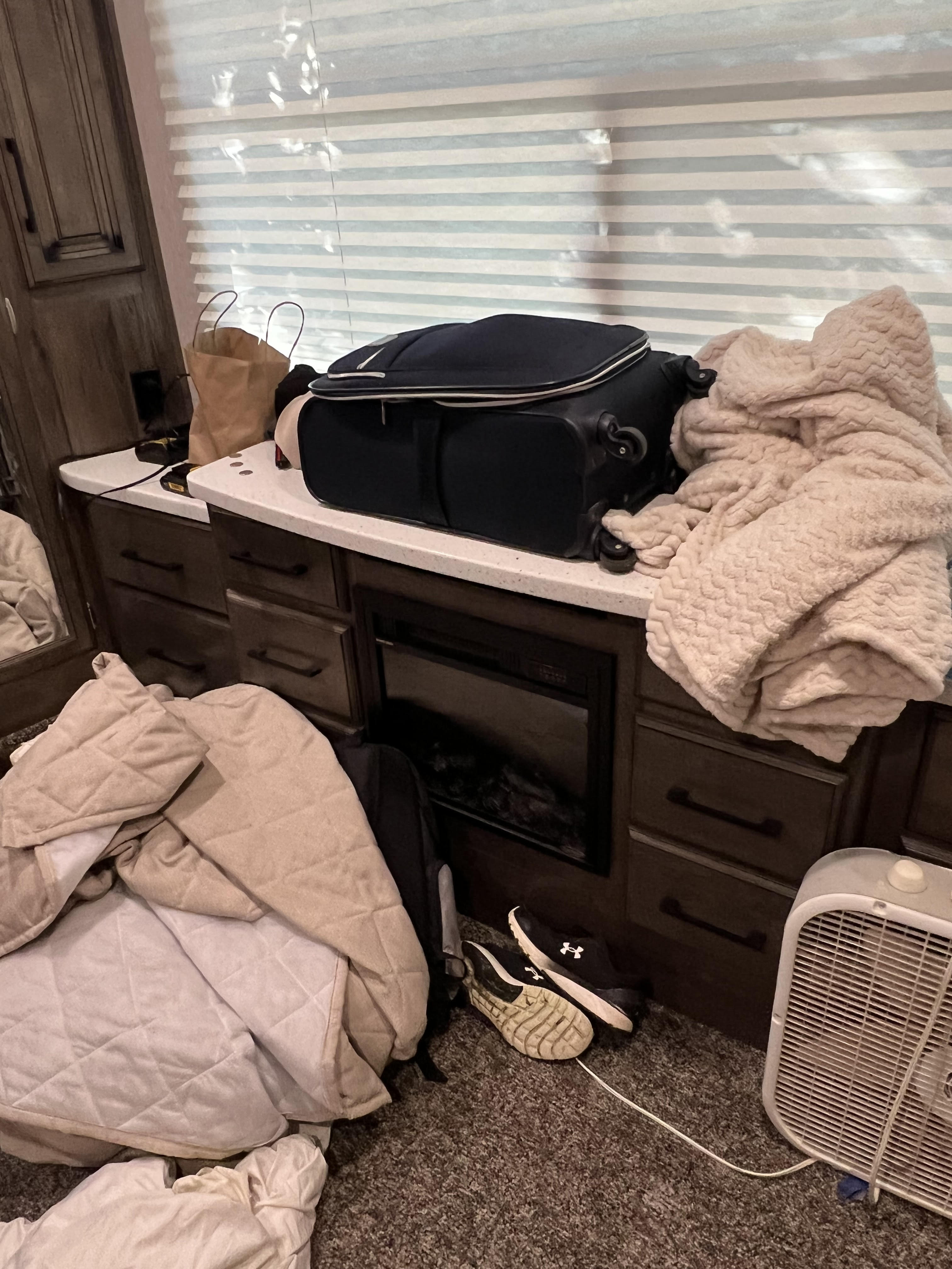 Inside an RV rental, a lived-in space with a large suitcase, blankets, fan, shoes, and an electric fireplace.. Heartland Cyclone 2019