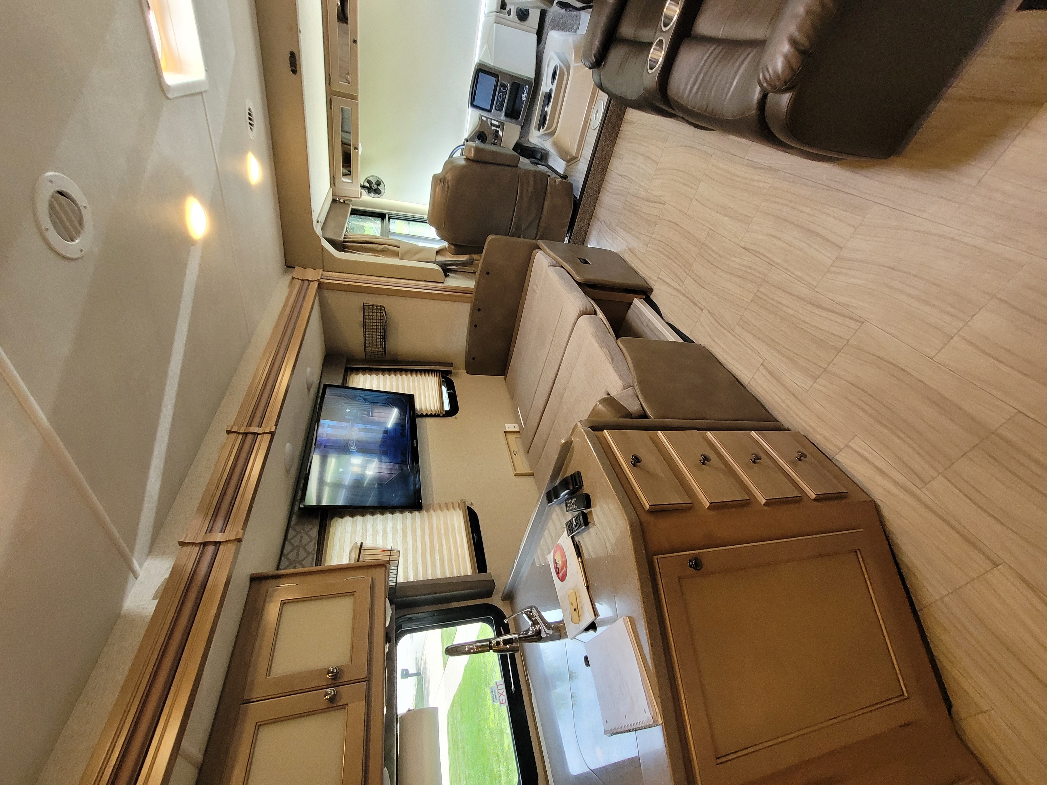 Spacious RV rental living area: recliners, sofa, TV, and kitchen. Features bright, modern design and wood-look flooring.. Thor Windsport 2019