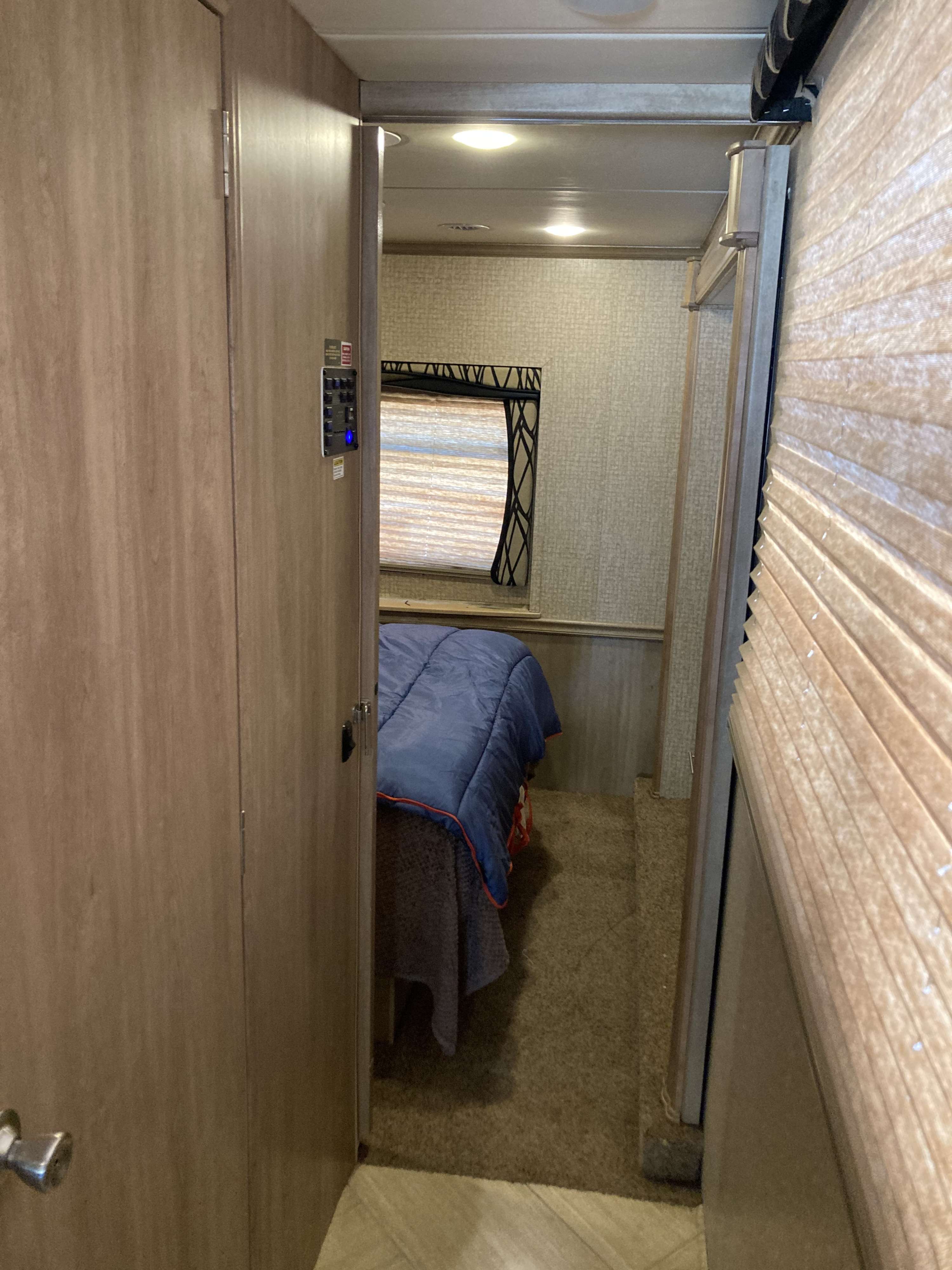 Inside an RV rental: a compact bedroom with a bed, blue comforter, window with blinds, and wall-mounted controls visible.. 1F66F5DY4E0A13513 37SA 2015
