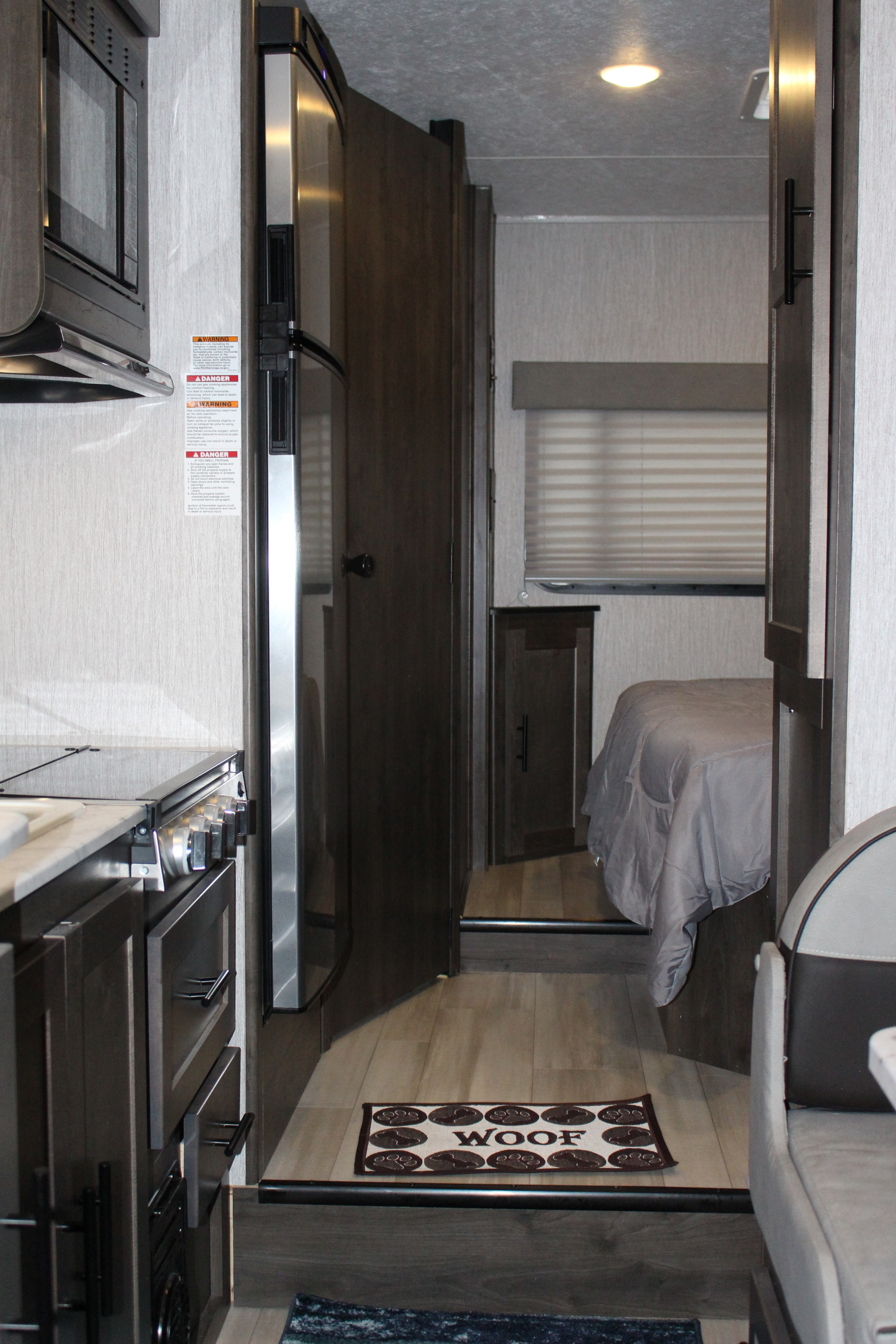 This RV rental interior showcases a compact kitchen, refrigerator, and a hallway leading to the bedroom, with a "WOOF" mat.. Forest River Coachmen Leprechaun 2022