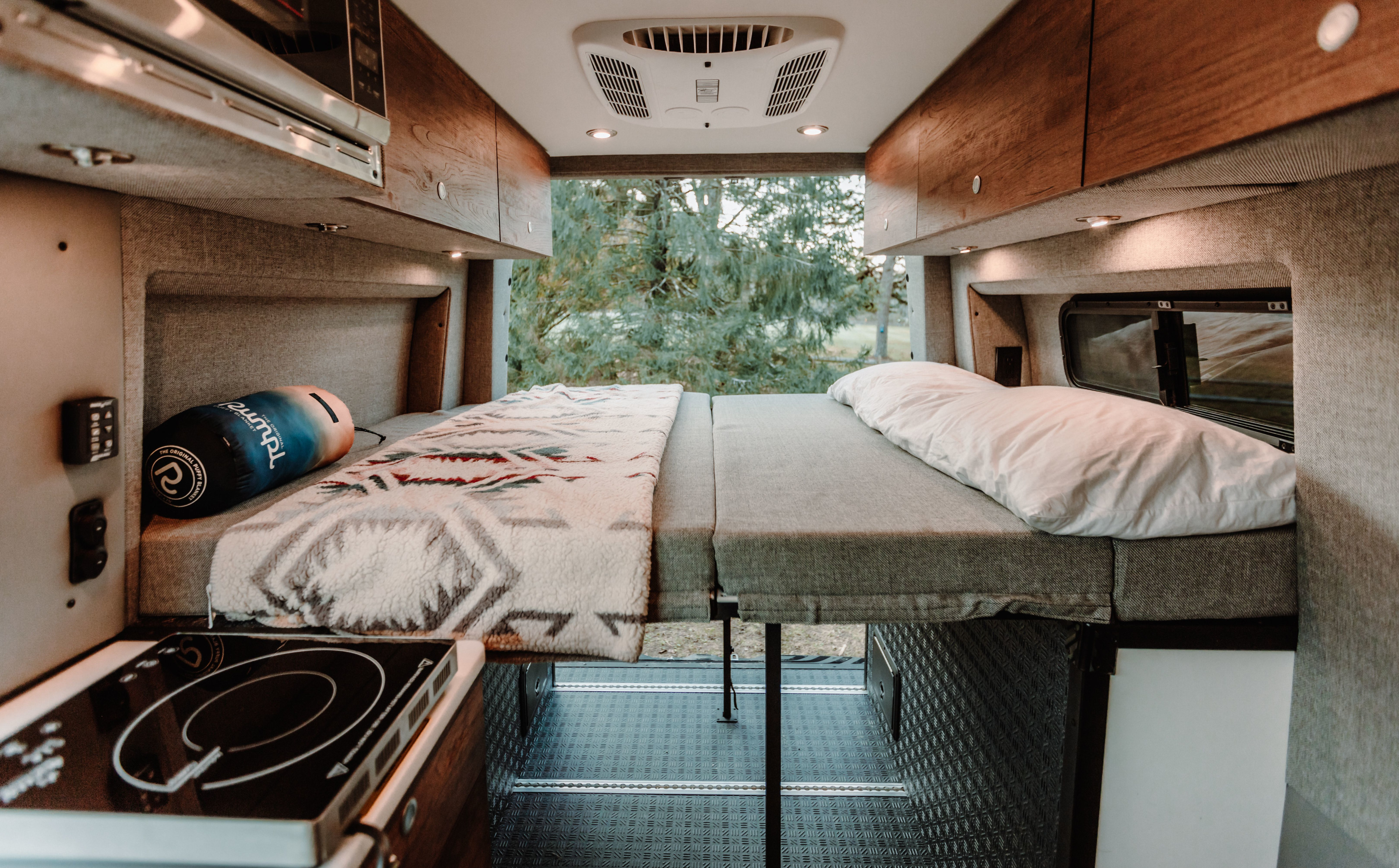 An RV rental's cozy interior, showing a modular bed, wood cabinets, and an induction cooktop. Ready for your adventure.. StoryTeller Overland Classic Mode 4X4 2022