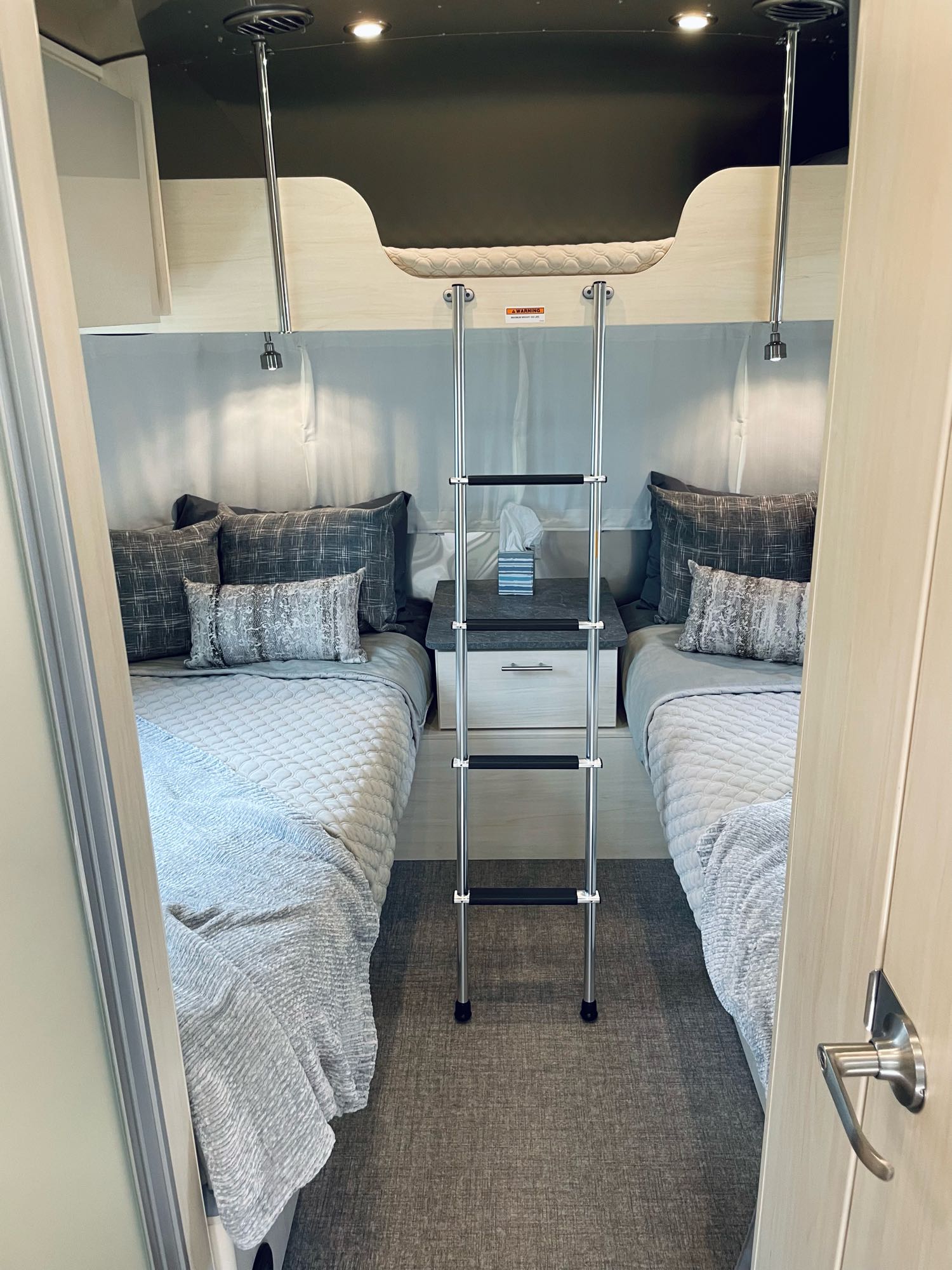 An RV rental bedroom featuring two twin beds, an overhead bunk with a ladder, and a central nightstand.. Airstream Flying Cloud 2022