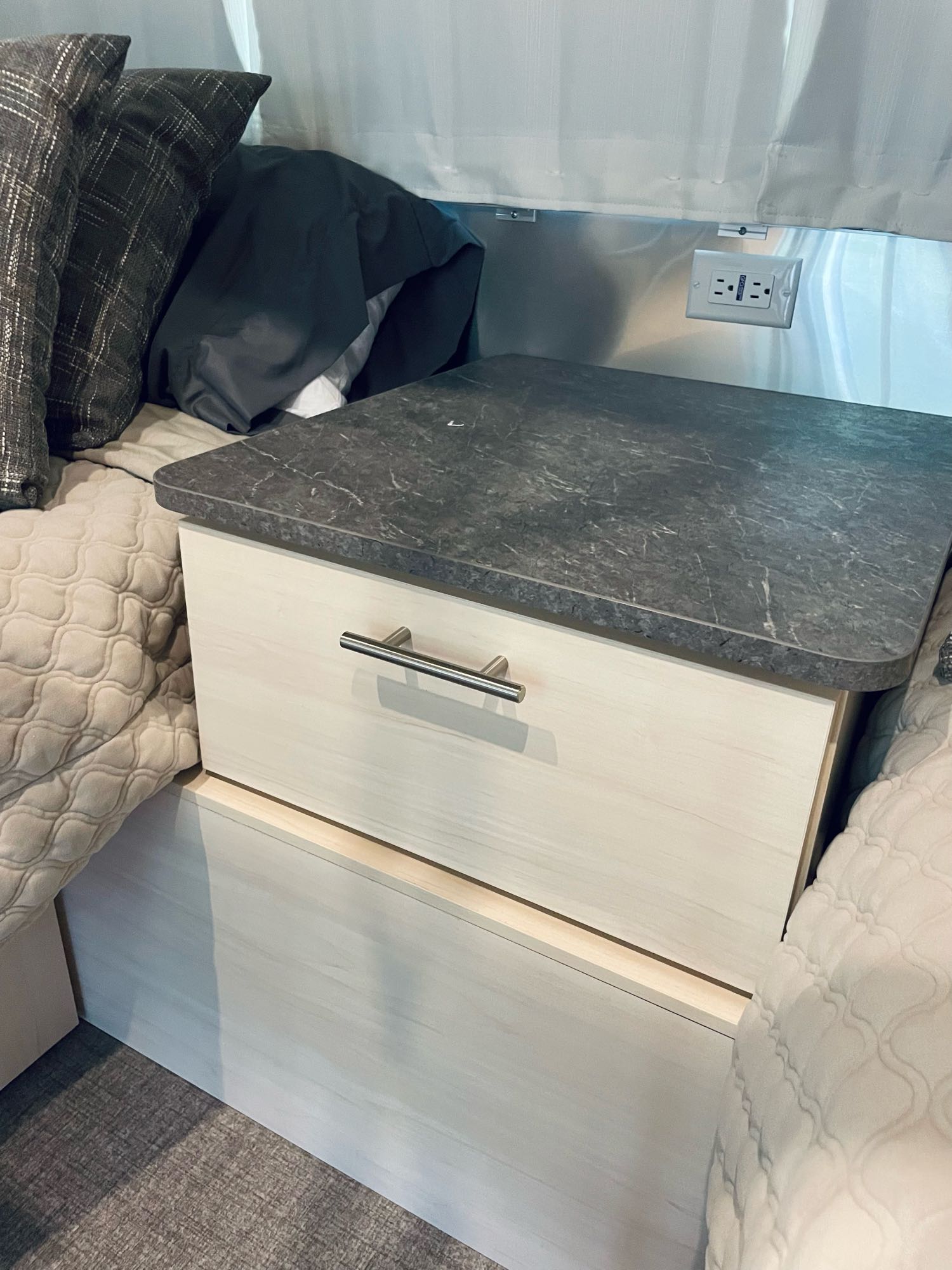 RV rental sleeping area featuring a nightstand with a marbled top, light wood drawer, and power outlet with USB.. Airstream Flying Cloud 2022