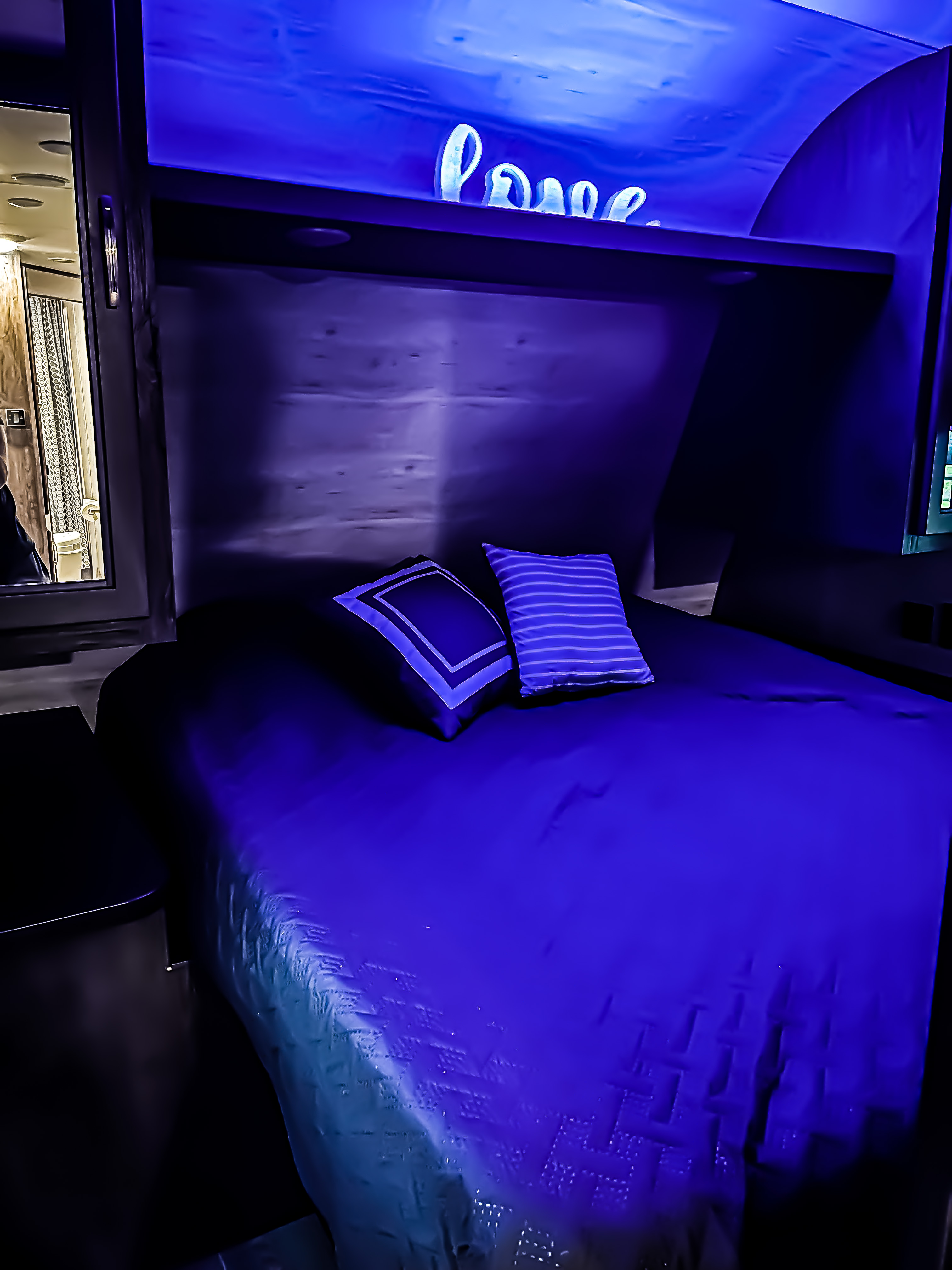 Cozy RV rental bedroom with a bed, blue lighting, and a glowing "love" sign, glimpsing a compact bathroom.. Jayco Jay Flight SLX 2021