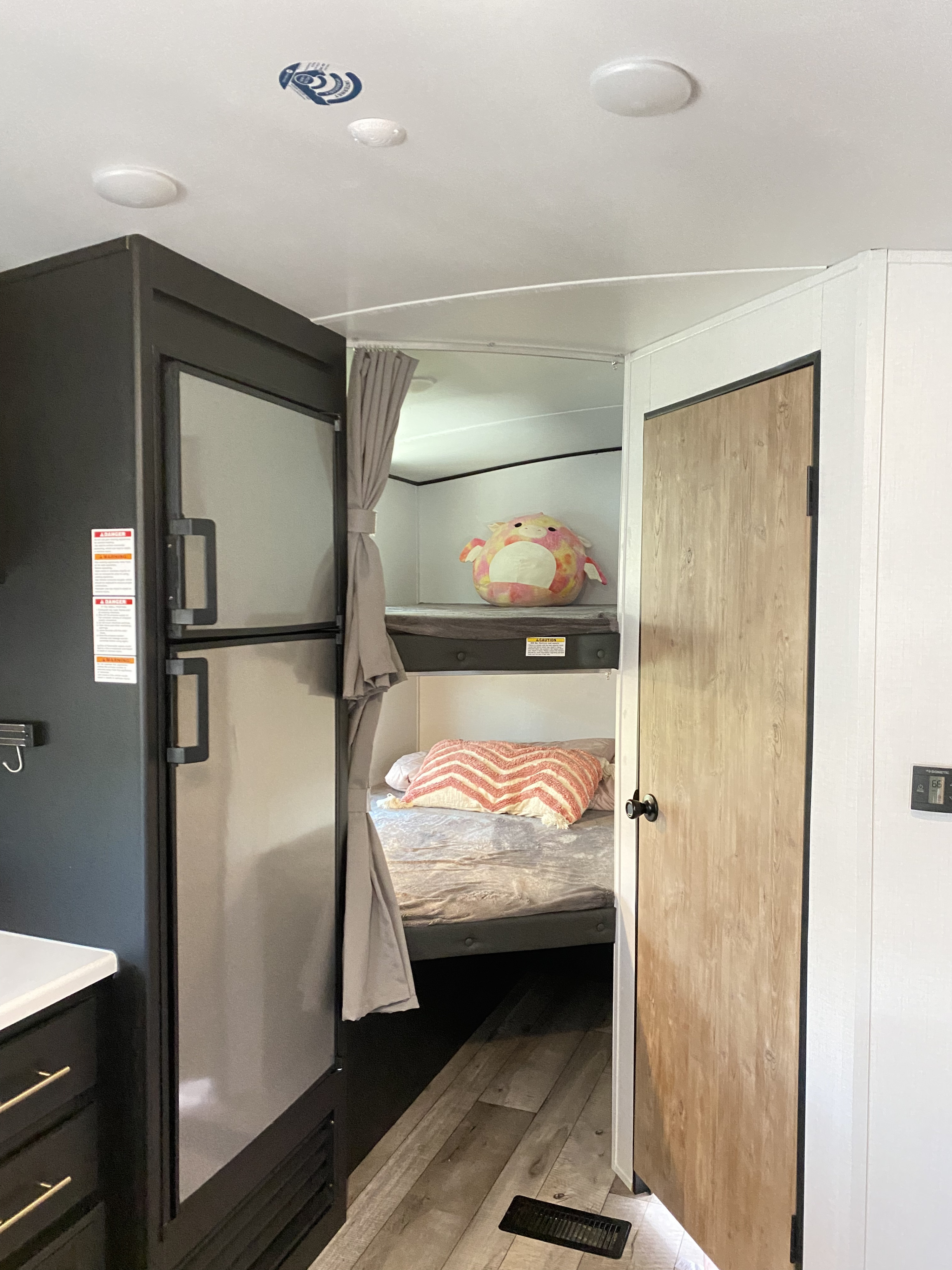 View inside an RV rental: modern kitchen with a large fridge, cozy bunk beds, and a light wood door. Perfect for travel.. Keystone RV Springdale 2022