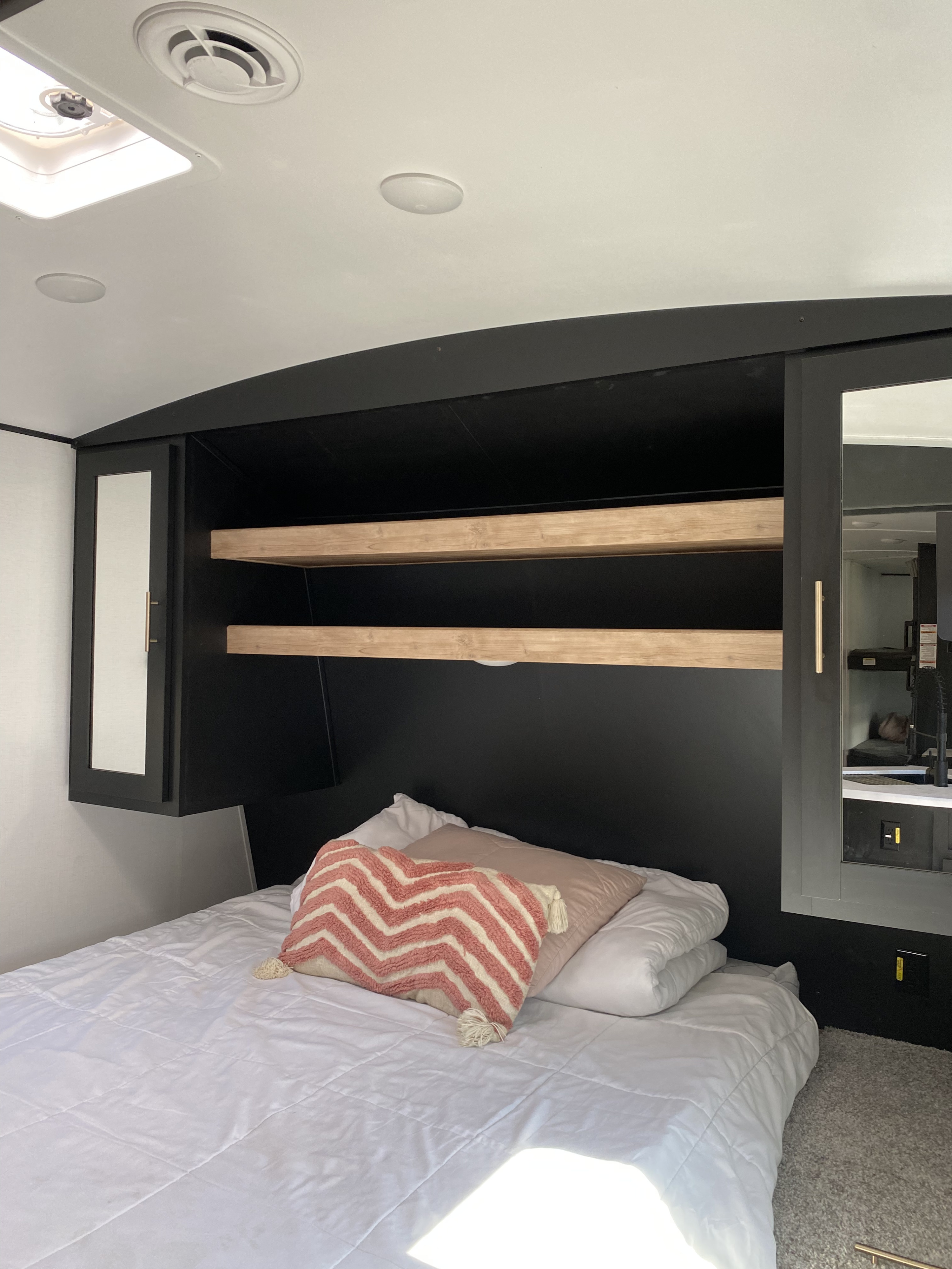 Cozy RV rental bedroom featuring a modern headboard with shelves and mirrored cabinets for organized travel.. Keystone RV Springdale 2022