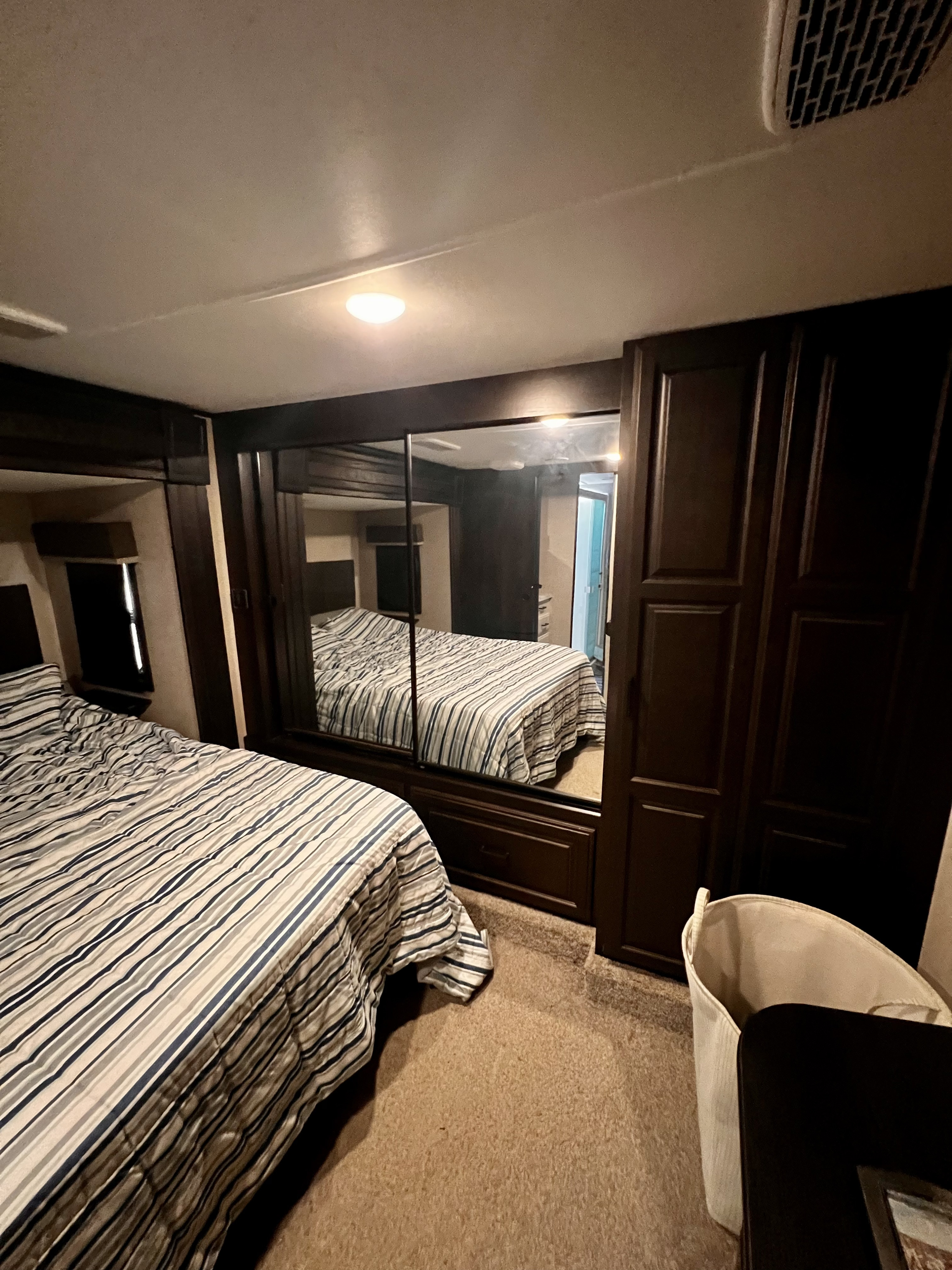 RV rental bedroom with a striped bed, large mirrored wardrobe, and ceiling vent, showing dark wood finishes.. Highland Ridge RV Open Range 2021