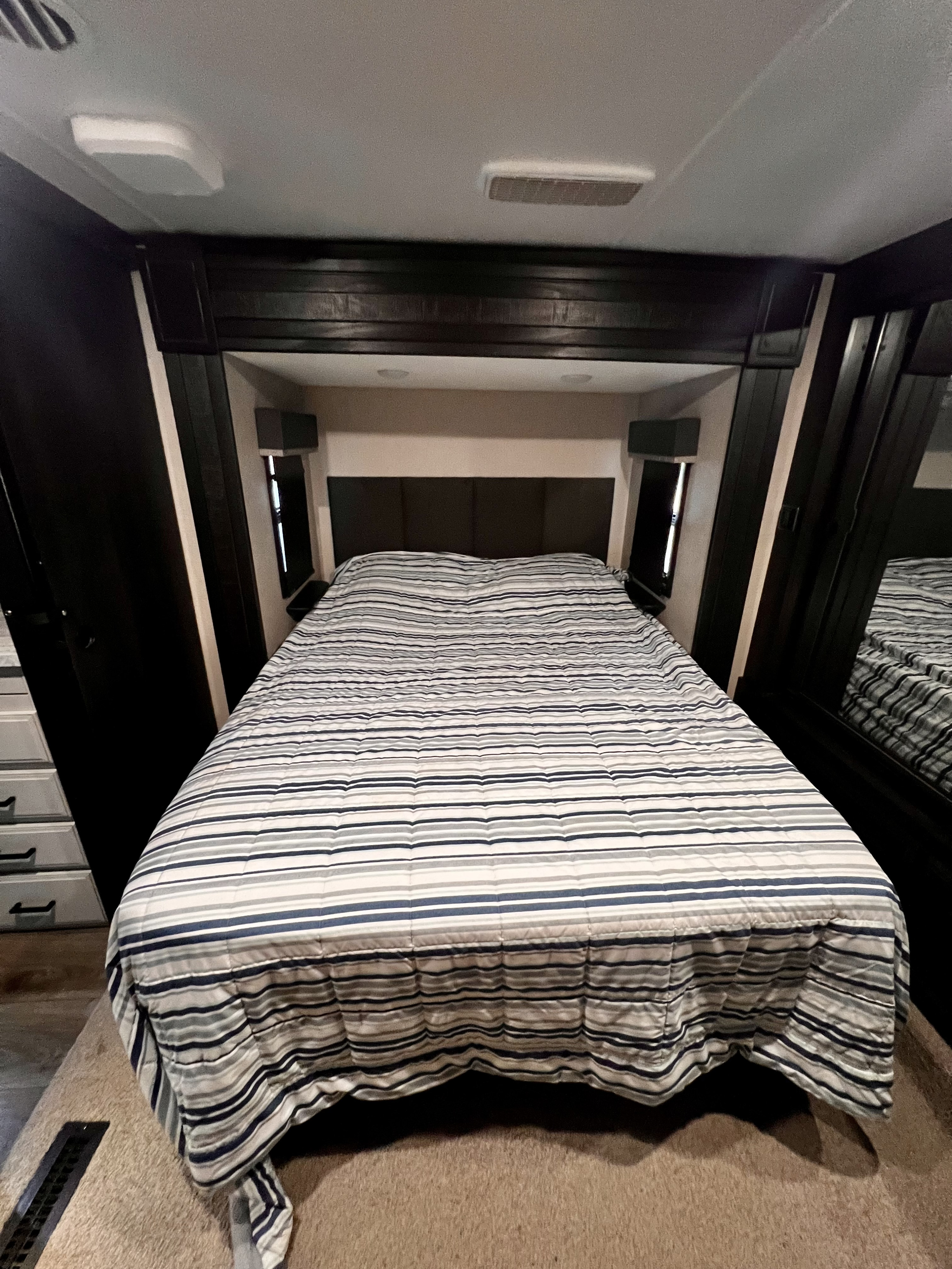 Comfortable RV rental bedroom with a striped comforter, built-in storage, and mirror. Perfect for travel!. Highland Ridge RV Open Range 2021