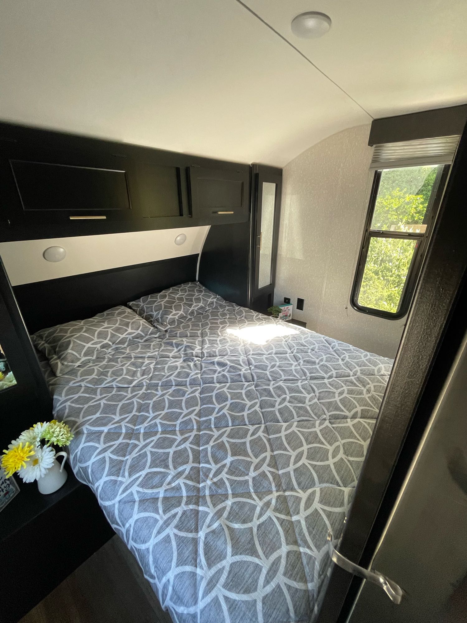 This RV rental bedroom features a comfy bed with grey patterned bedding, overhead cabinets, and a window.. Forest River Cherokee Grey Wolf 2022