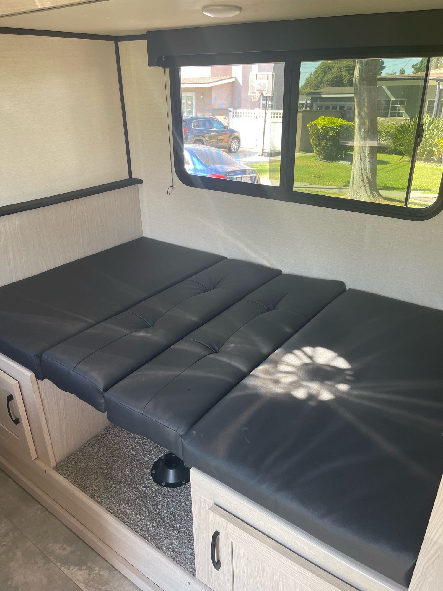 Inside this RV rental: a black cushioned dinette converts to a bed, with light wood storage and large windows.. Forest River Coachman Apex Nano 2022
