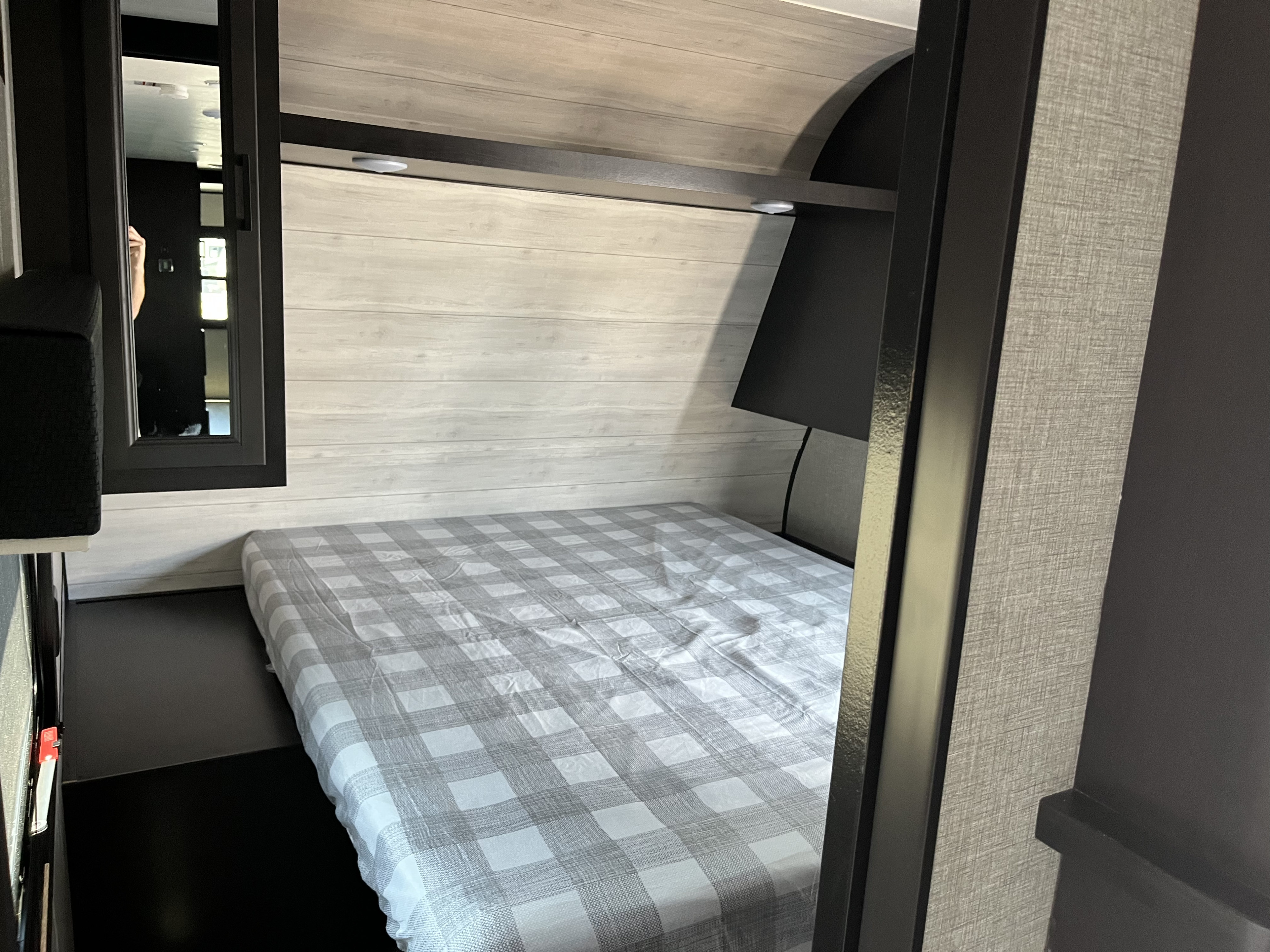 Inside an RV rental, this cozy bedroom features a bed with plaid sheets, a built-in headboard with lights, and a mirror.. Jayco Jay Flight SLX 2022