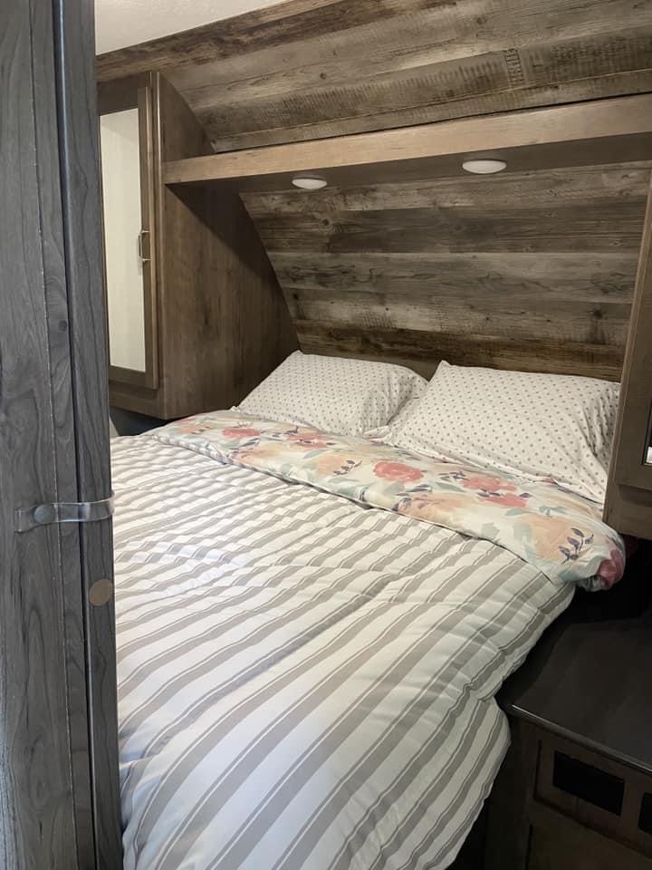 Experience comfort in your RV rental. This cozy bedroom has a striped bed, wood interior, and practical overhead lighting.. Keystone Passport 2020