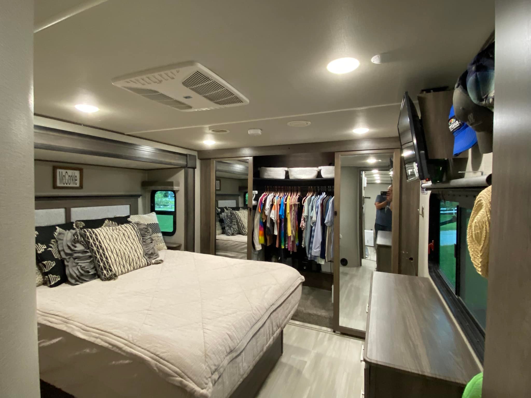 Inside a modern RV rental bedroom featuring a spacious bed with pillows, an open closet, and mounted TV.. Grand Design Solitude 2021
