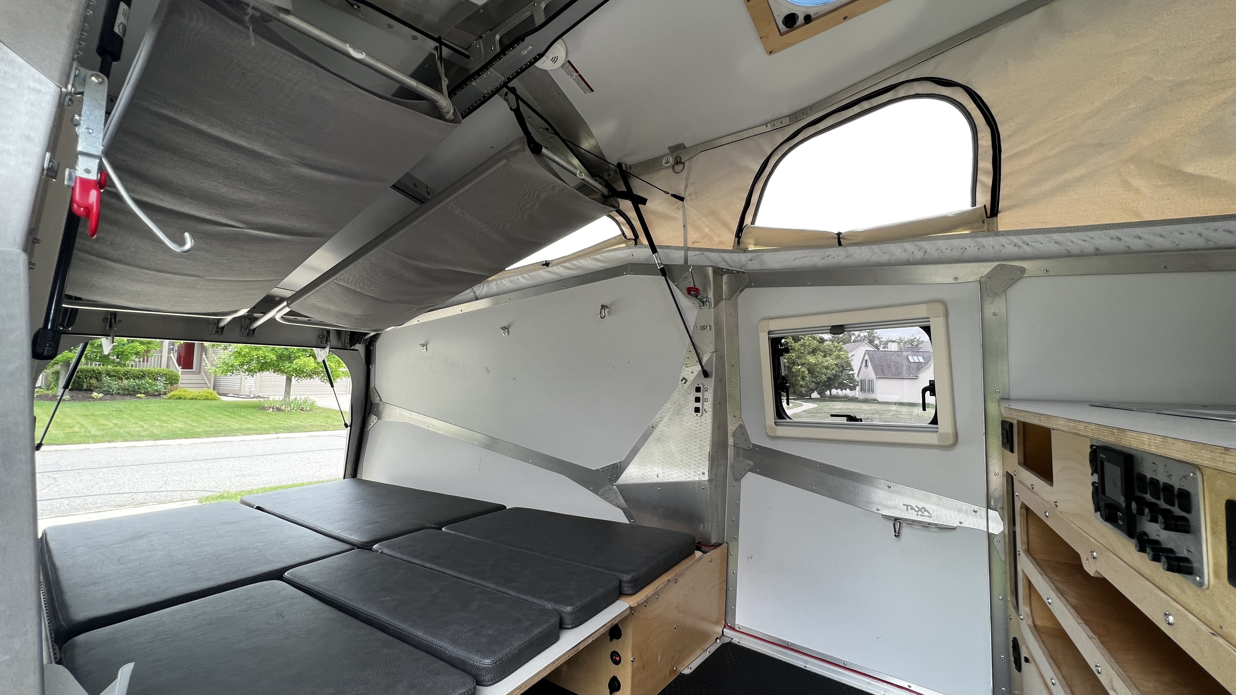 Compact RV rental interior featuring a convertible bed, pop-up roof, and organized controls. Ideal for outdoor adventures.. TAXA Cricket Overland Edition 2020