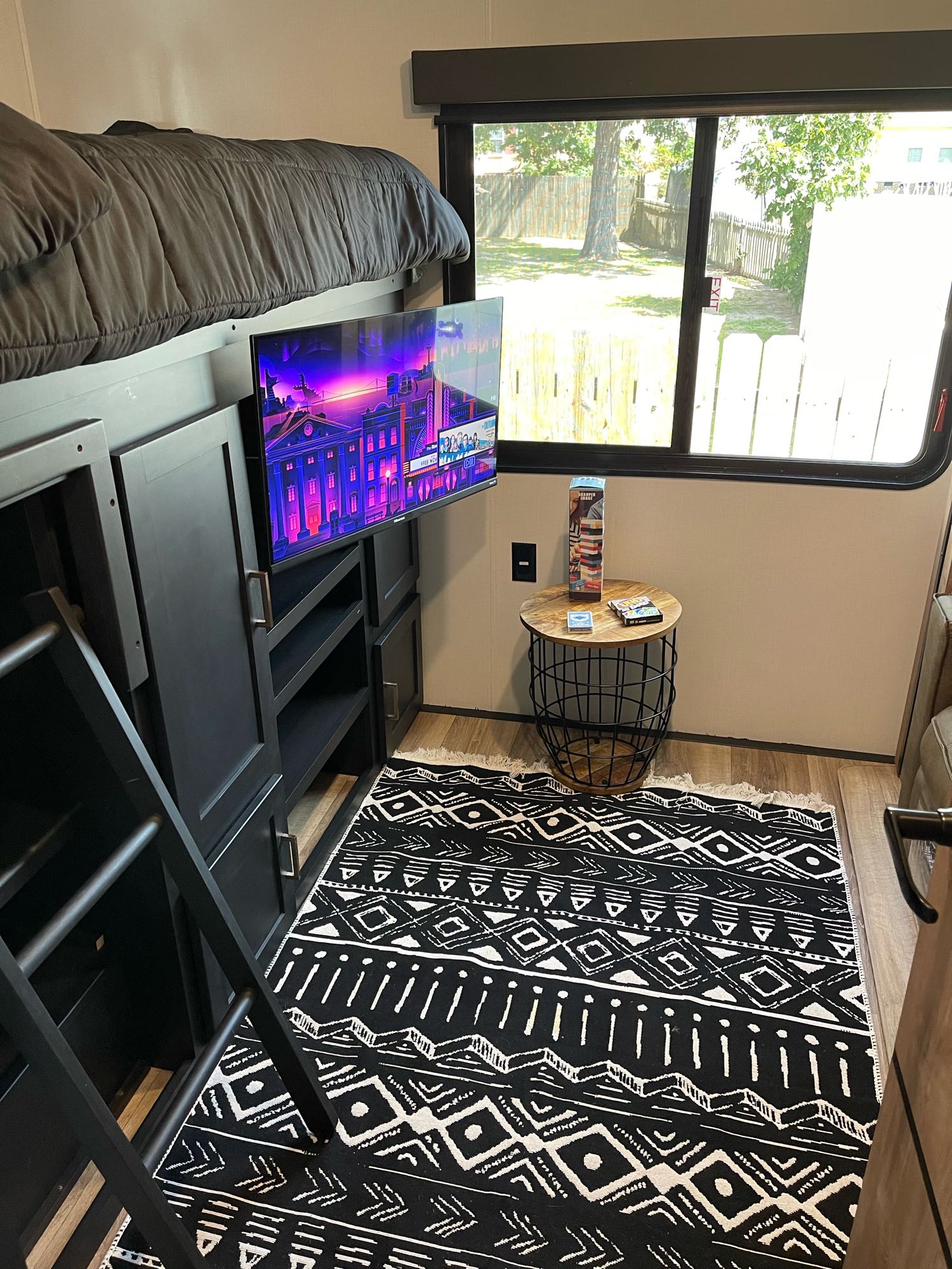 Step inside this RV rental, featuring a cozy bunk bed, wall-mounted TV, built-in storage, and a black patterned rug.. Keystone RV Outback 2022