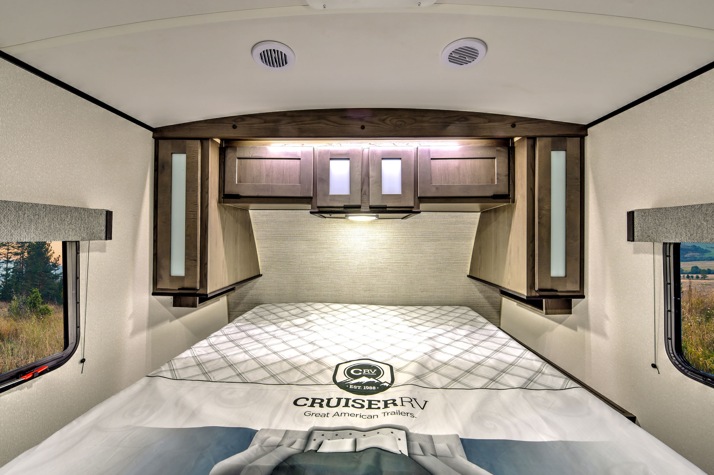 Cozy RV rental bedroom with overhead storage, soft lighting, and window views for a comfortable journey.. Cruiser RV MPG Ultra Lite 2022