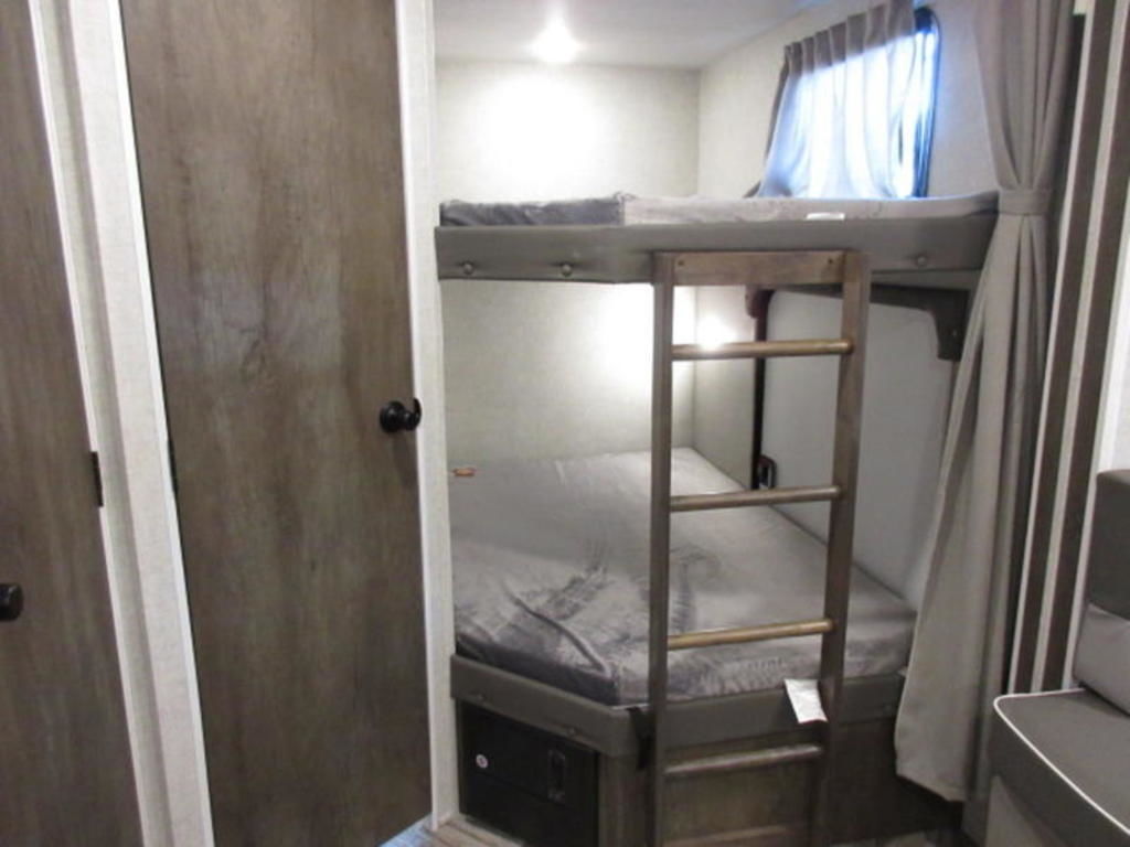 View of an RV rental's bunk bed area: two beds, a wooden ladder, and a window with curtains.. Forest River Wildwood 2021