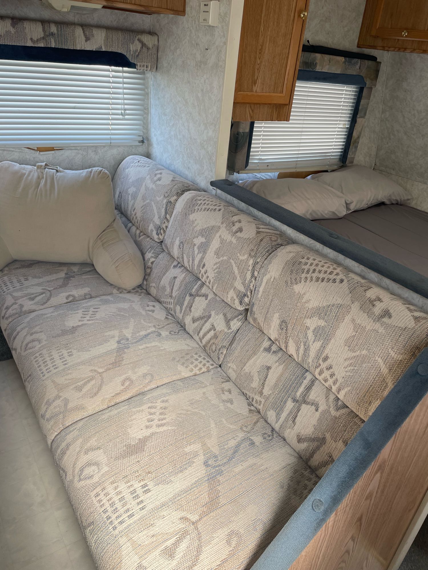 This RV rental interior shows a patterned sofa, pillows, and a bed in a living/sleeping area with blinds.. Thor Wanderer 2001